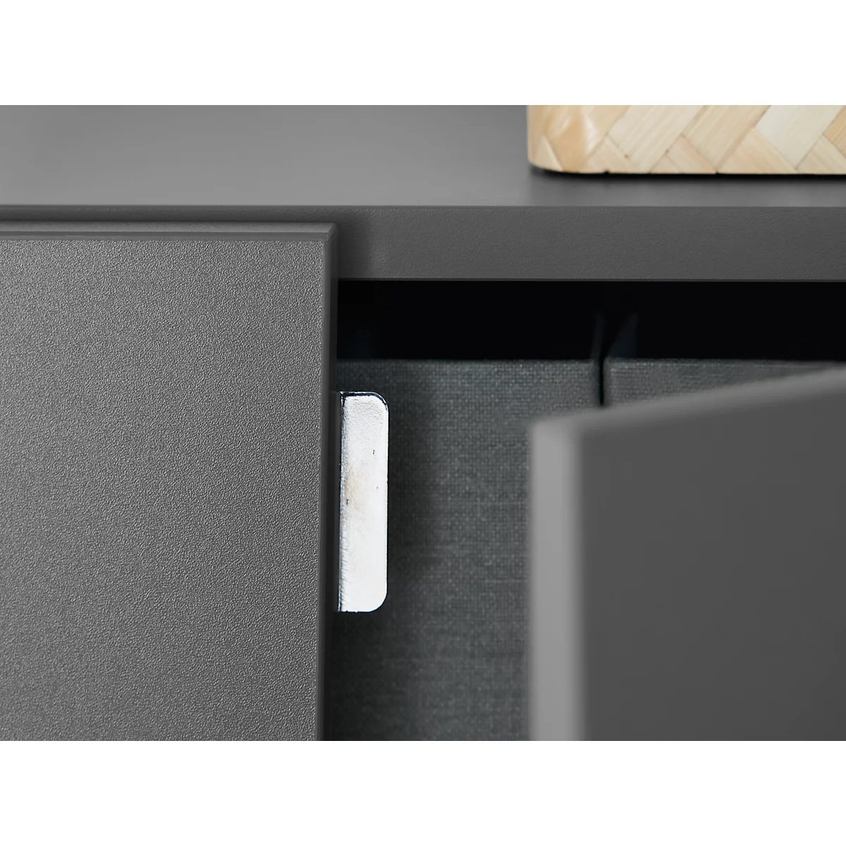 Close-up of a grey furniture edge with a silver hinge. A door is half open.