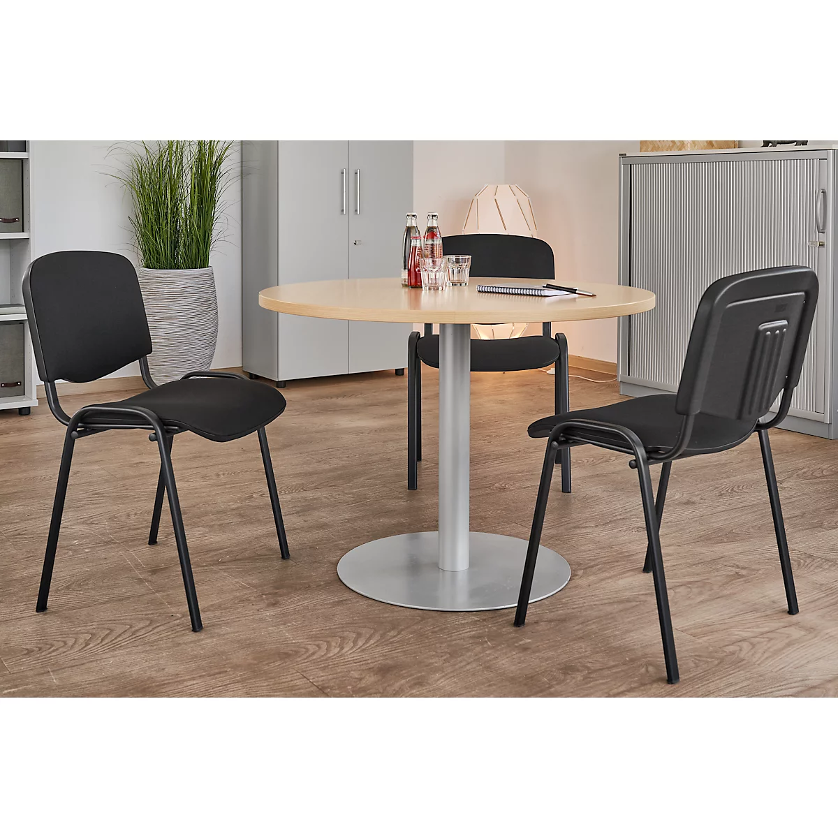 A round table with three chairs in an office. Drinks and a notepad are on the table.