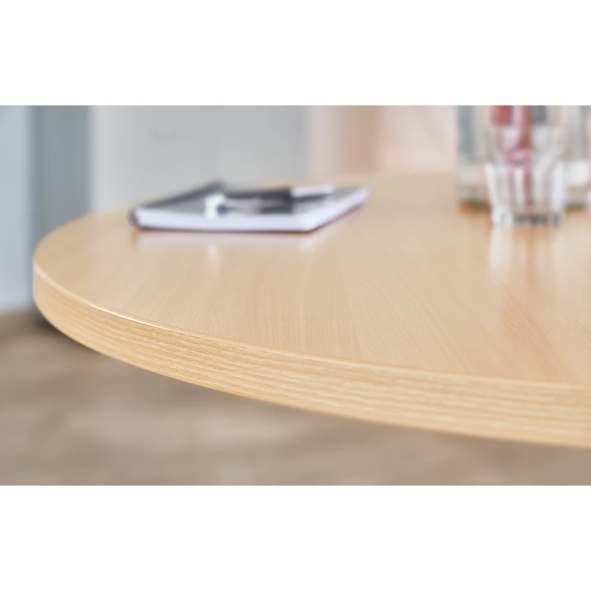 Light brown, round table with notebook and pen. Glasses in the background.