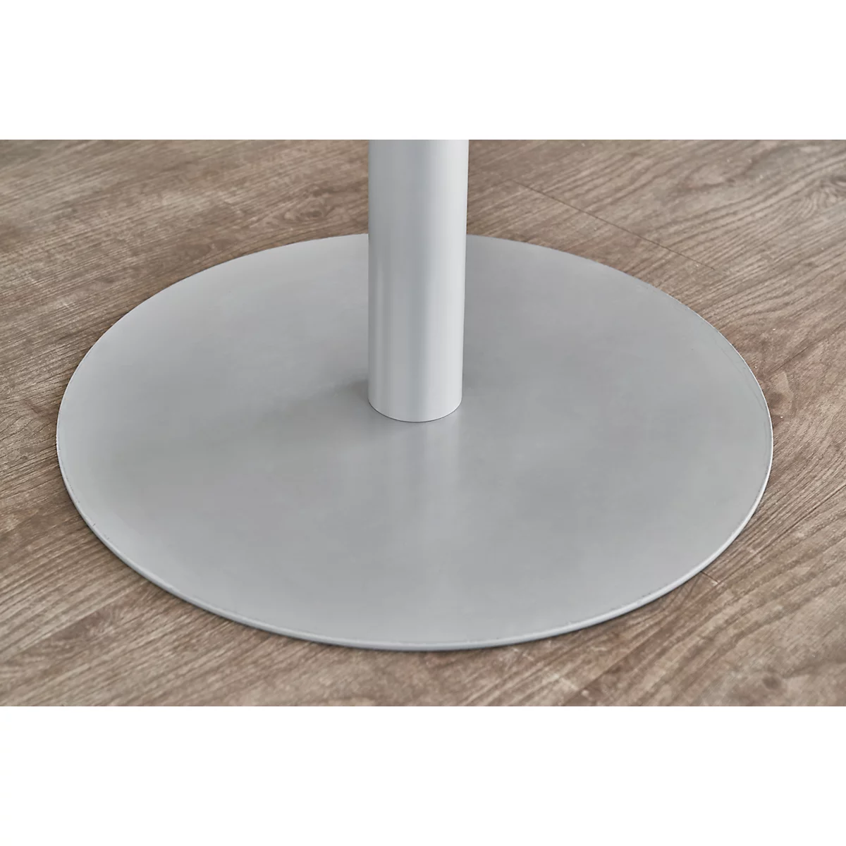 Close-up of a white table base with a round, gray base on a light wooden surface.