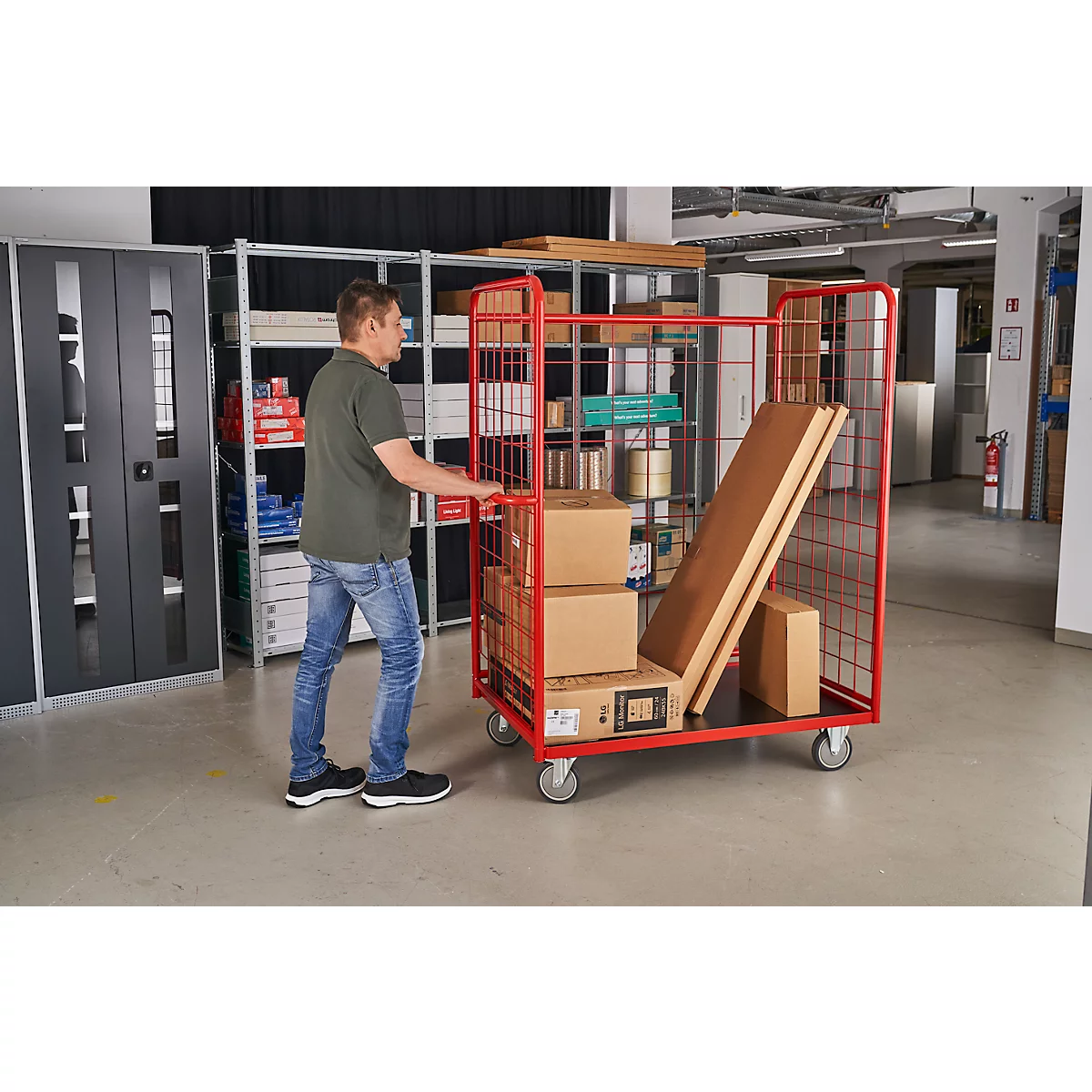 A man pushing a red trolley with boxes through a warehouse. The cart is loaded with goods.