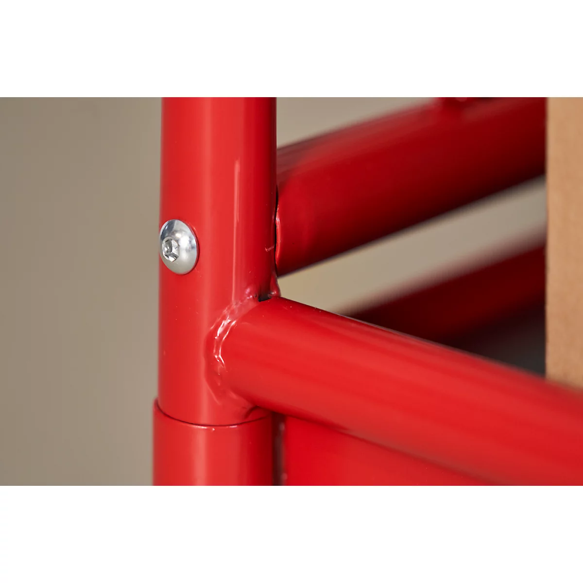Close-up of a red metal construction, fastened with a screw. The background is light beige.