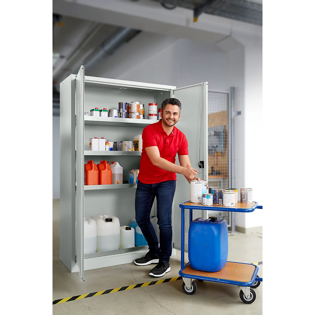 Mann steht vor einem Stahlschrank, ergreift Farbe von einem Wagen. Schrank mit Farben, Gebinden gefüllt.