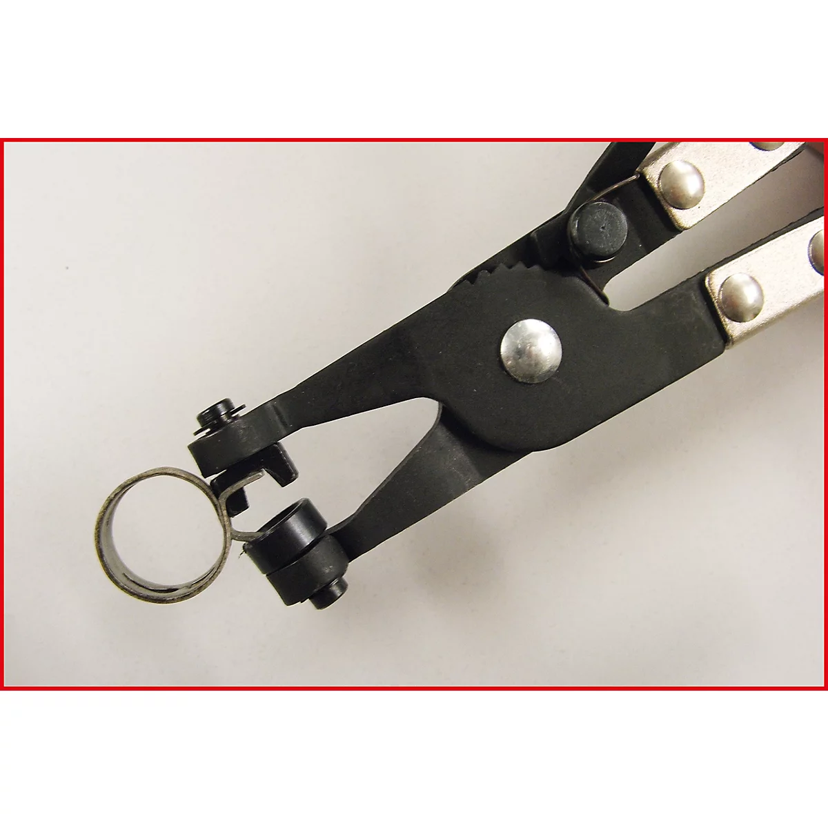 Nahaufnahme einer schwarzen Sprengringzange, die einen Metallring hält. Der Hintergrund ist weiß.
