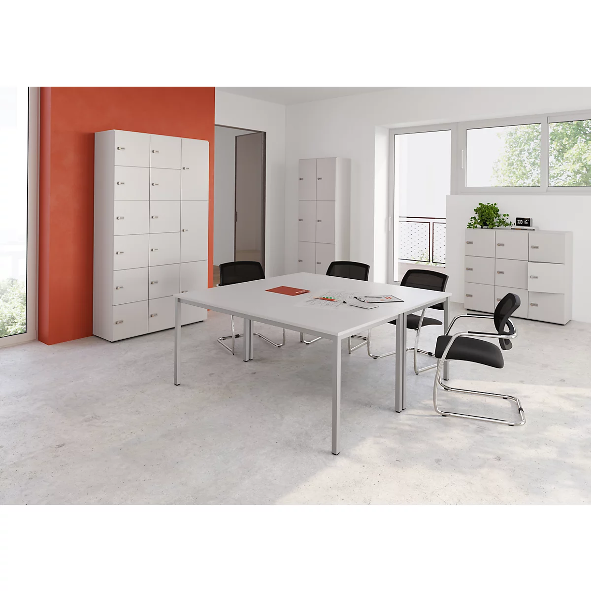 Ein heller Büroraum mit weissem Tisch, Stühlen und Schränken. Orangefarbene Wand. Blick durch ein Fenster ins Freie.