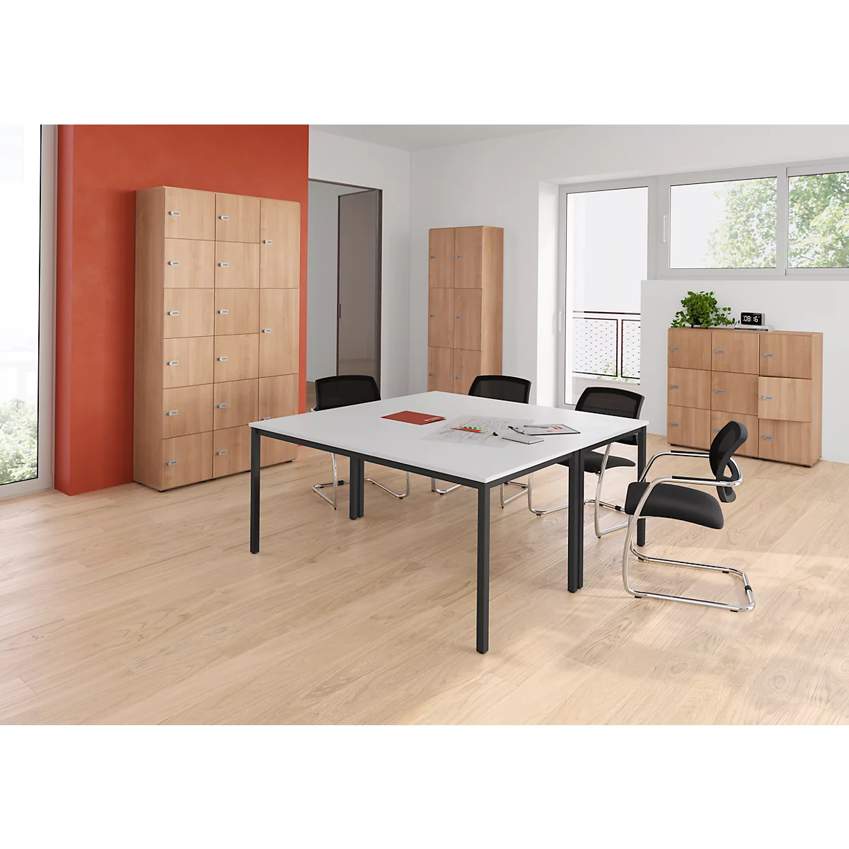 Ein Büro mit Holzböden, weissem Tisch, schwarzen Stühlen und Schränken. Ein Fenster lässt Tageslicht herein.