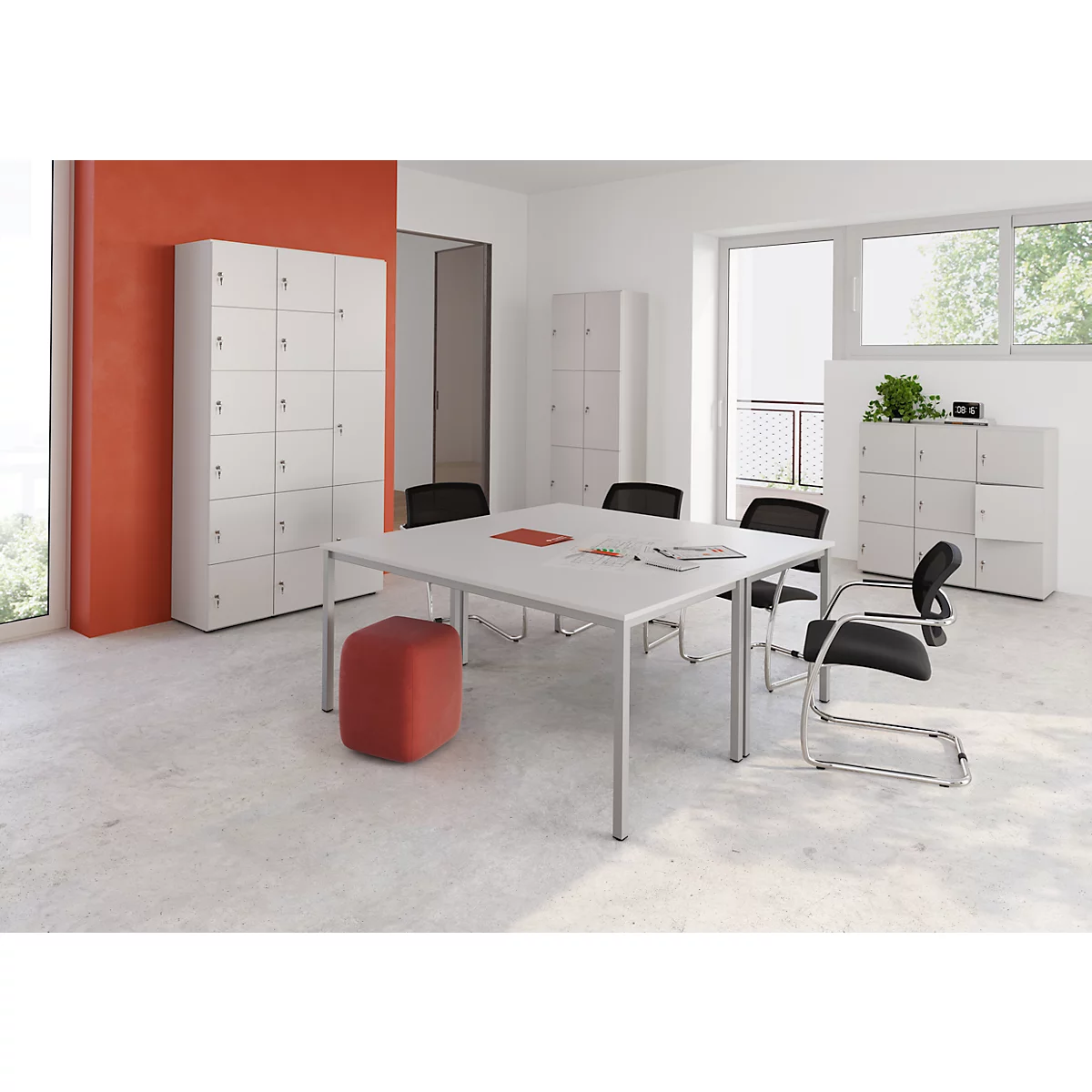 Ein heller, moderner Büroraum mit Tisch, Stühlen und Schränken. Ein roter Hocker steht daneben. Fenster mit Tageslicht.