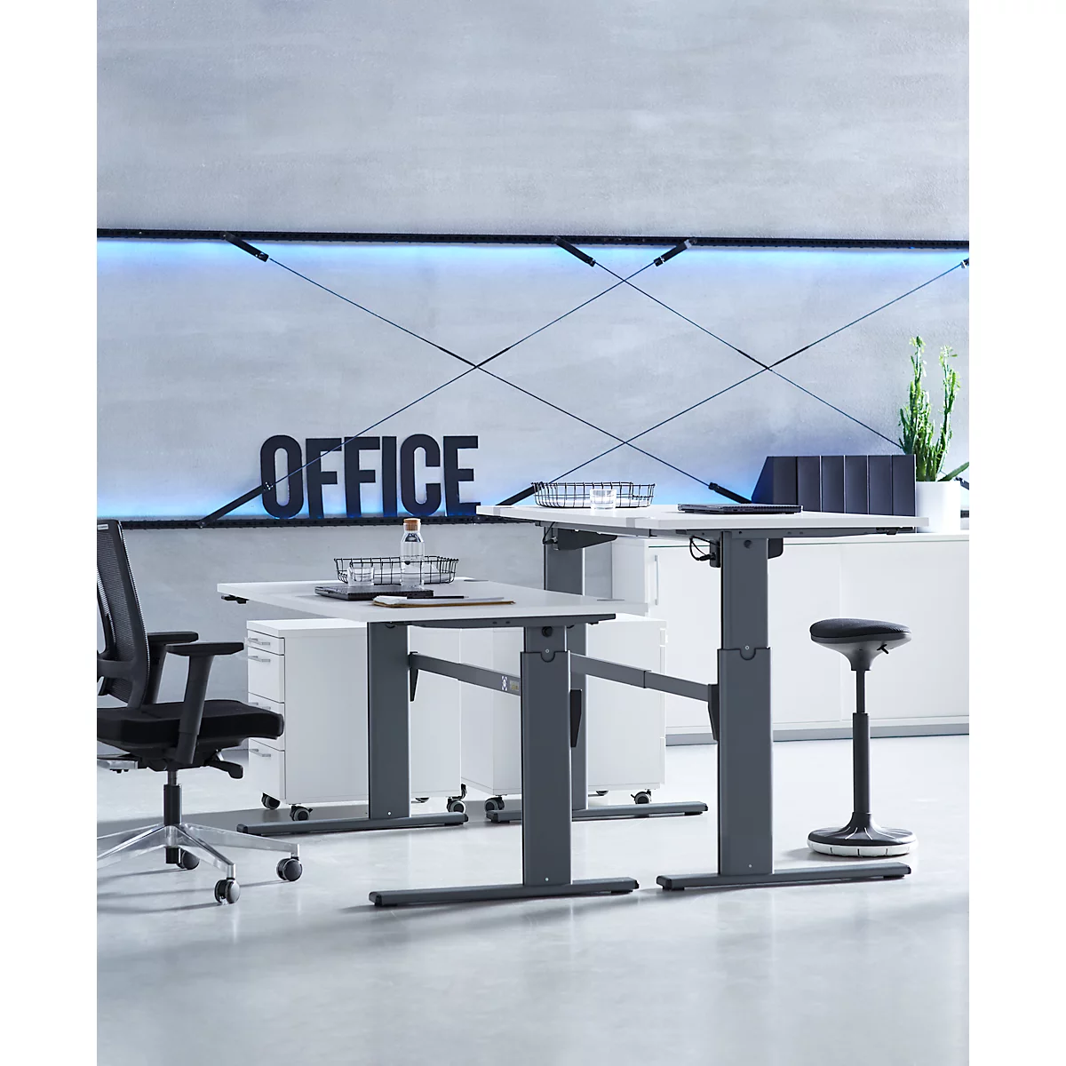 Zwei höhenverstellbare Schreibtische in einem modernen Büro vor einer Wand mit dem Schriftzug Office.