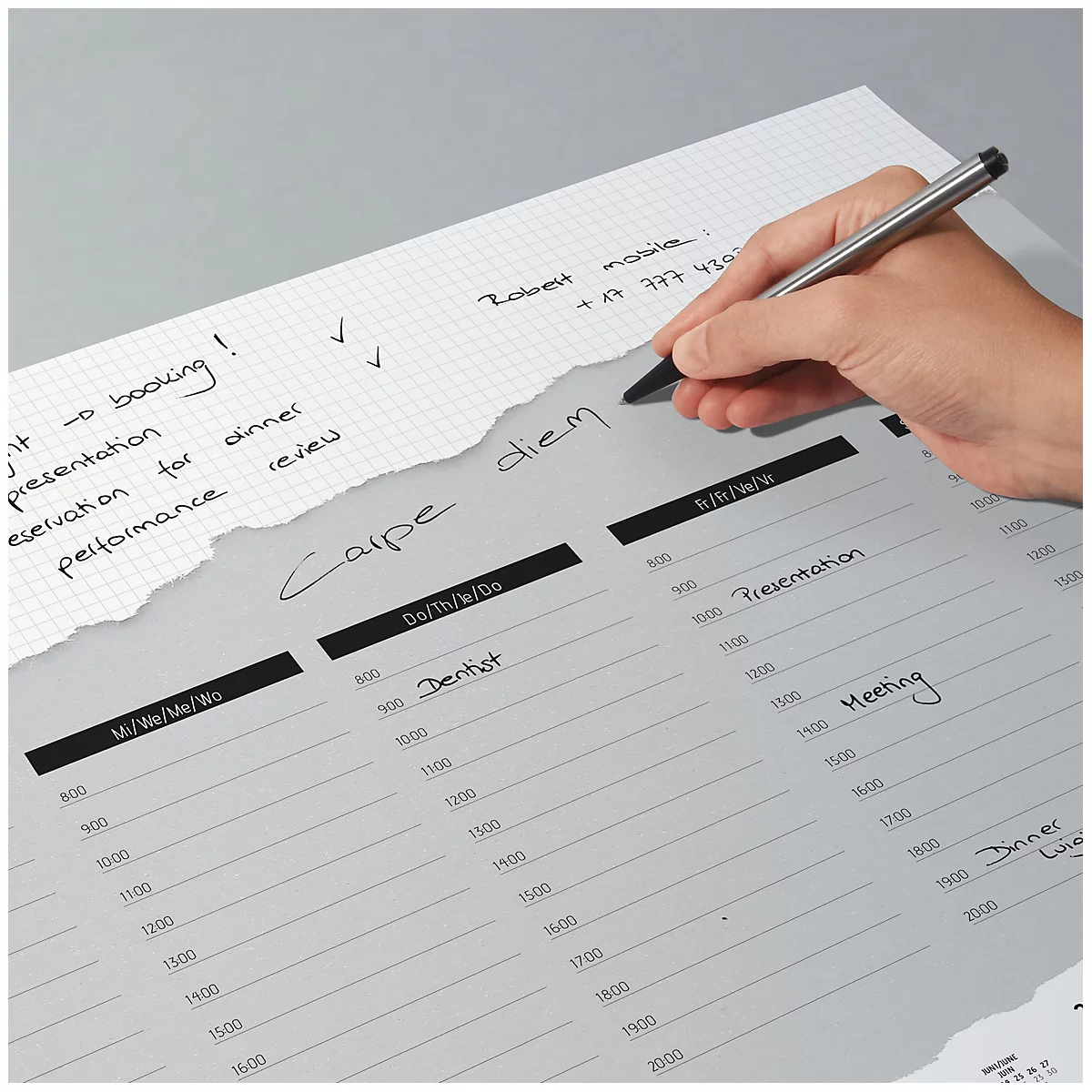 Eine Hand mit Stift beschreibt einen grauen, perforierten Wochenplaner. Der Planer ist mit handschriftlichen Notizen versehen, wie z.B. "Carpe diem".