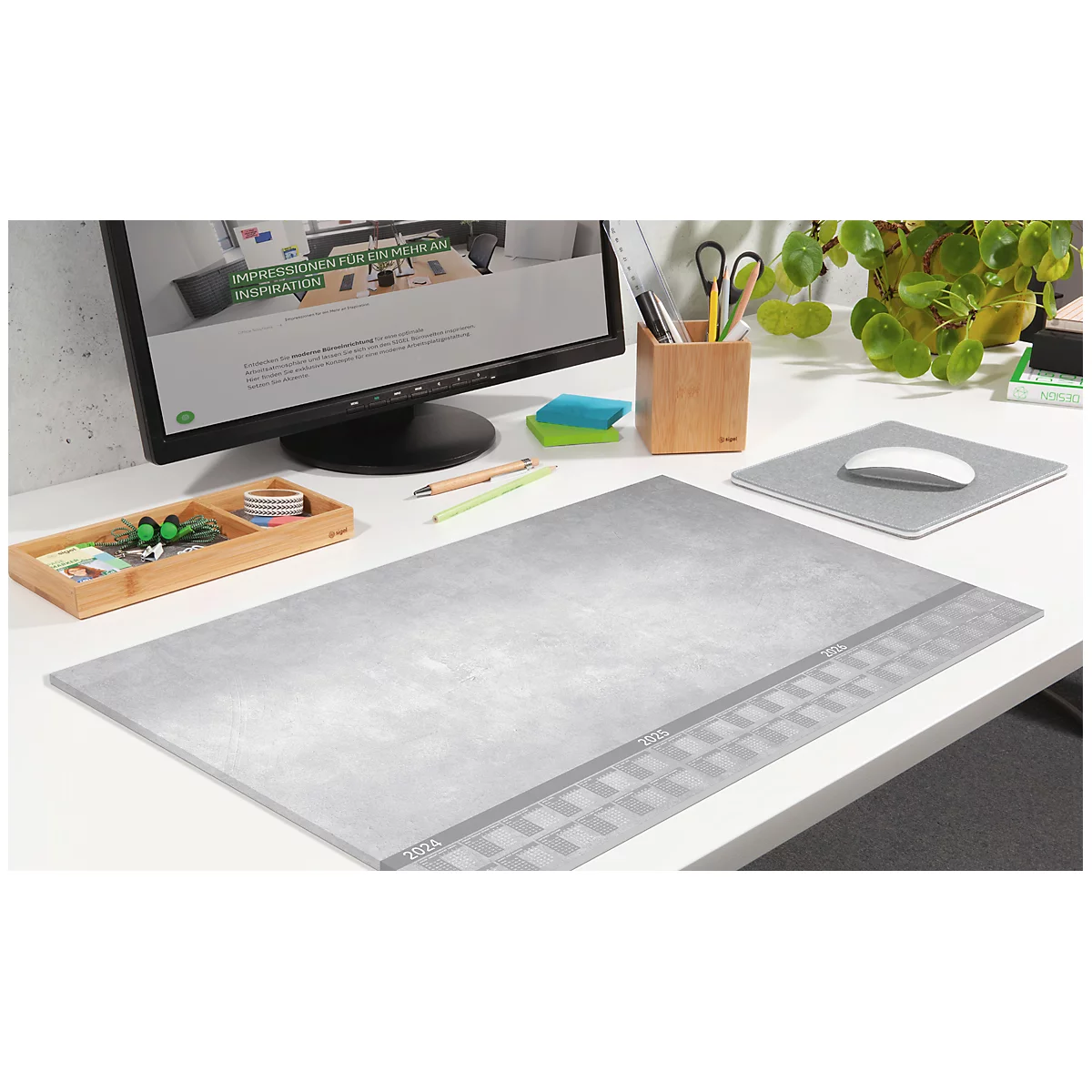 Graue Schreibtischunterlage auf einem weißen Tisch mit Computer, Stifthalter und Pflanze. Details im Textil Design.