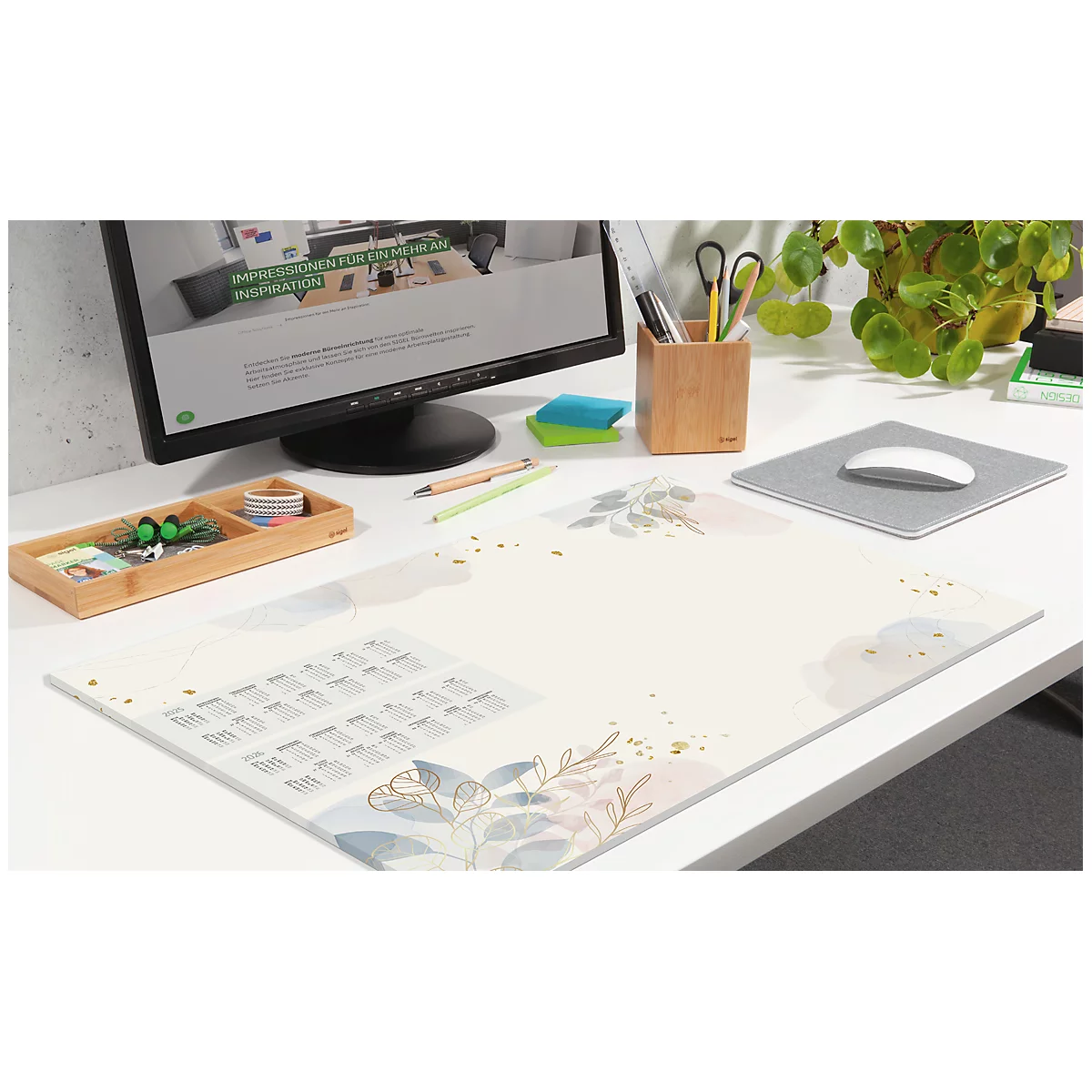 Schreibtisch mit einer Schreibtischunterlage mit Pflanzenmotiv, Computer, Stiftehalter und Mauspad.
