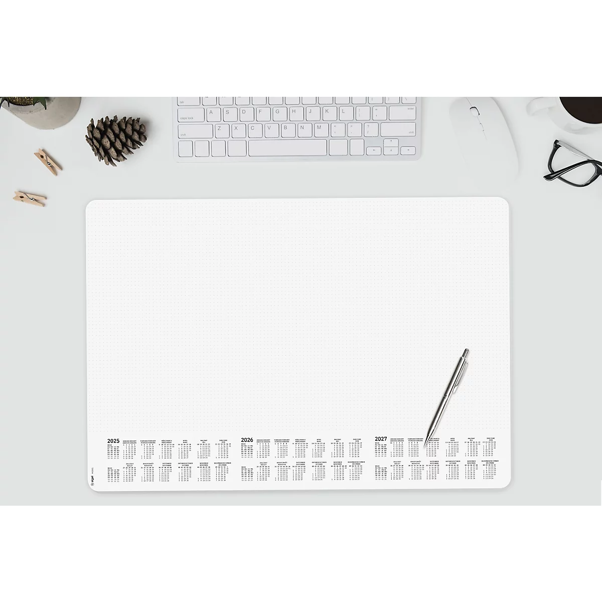 Schreibtischunterlage mit Jahreskalender, Stift, Tastatur, Maus, Brille, Tasse, Tannenzapfen und Deko-Klammern.
