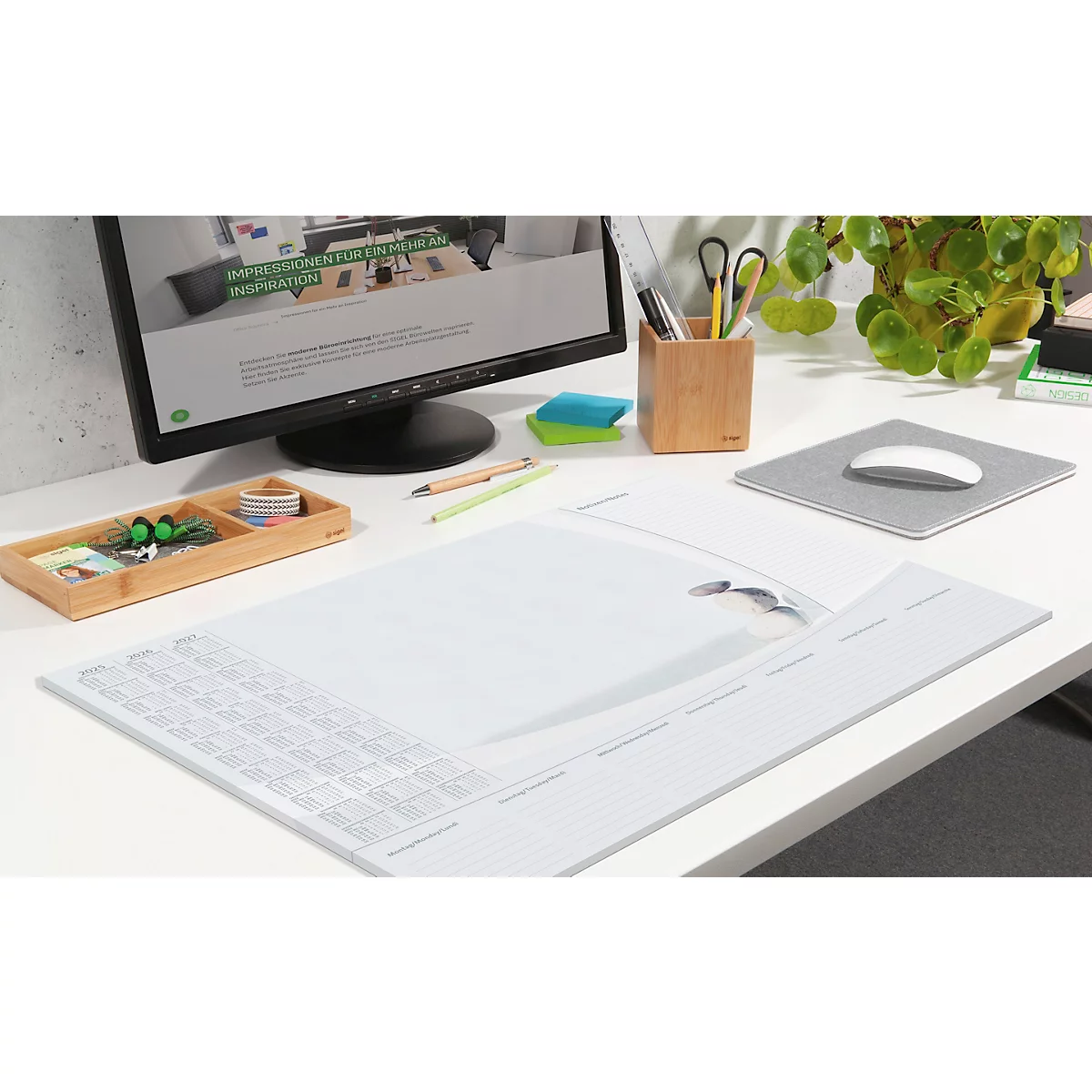 Weisser Schreibtisch mit Monitor, Mauspad, Stifthalter, Bambusbox und Pflanzen. Ein Produkt liegt als transparente Auflage darauf.