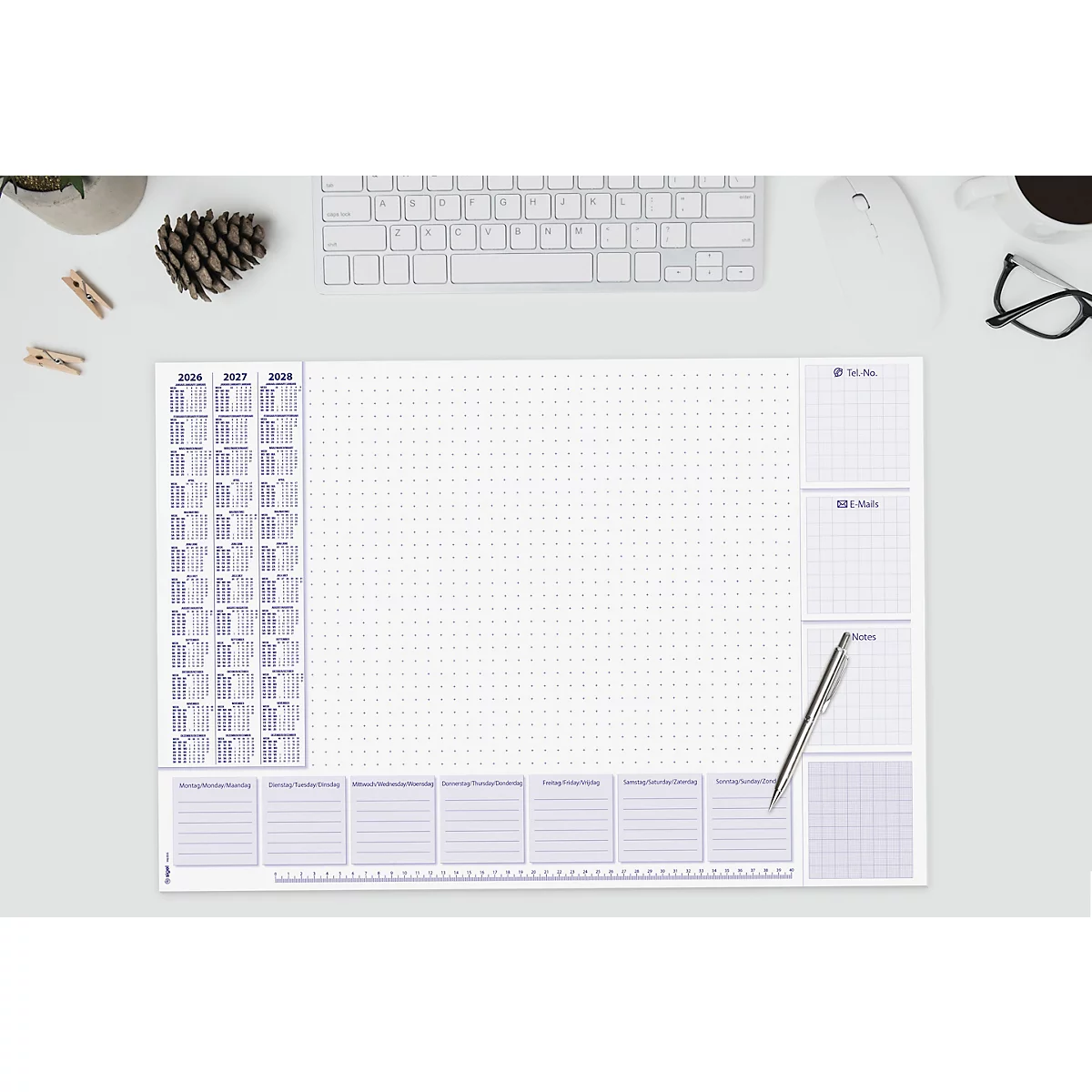 Schreibtischunterlage mit Kalender und Wochenübersicht. Kugelschreiber liegt auf der rechten Seite. Weitere Gegenstände: Tastatur, Brille, Tasse.