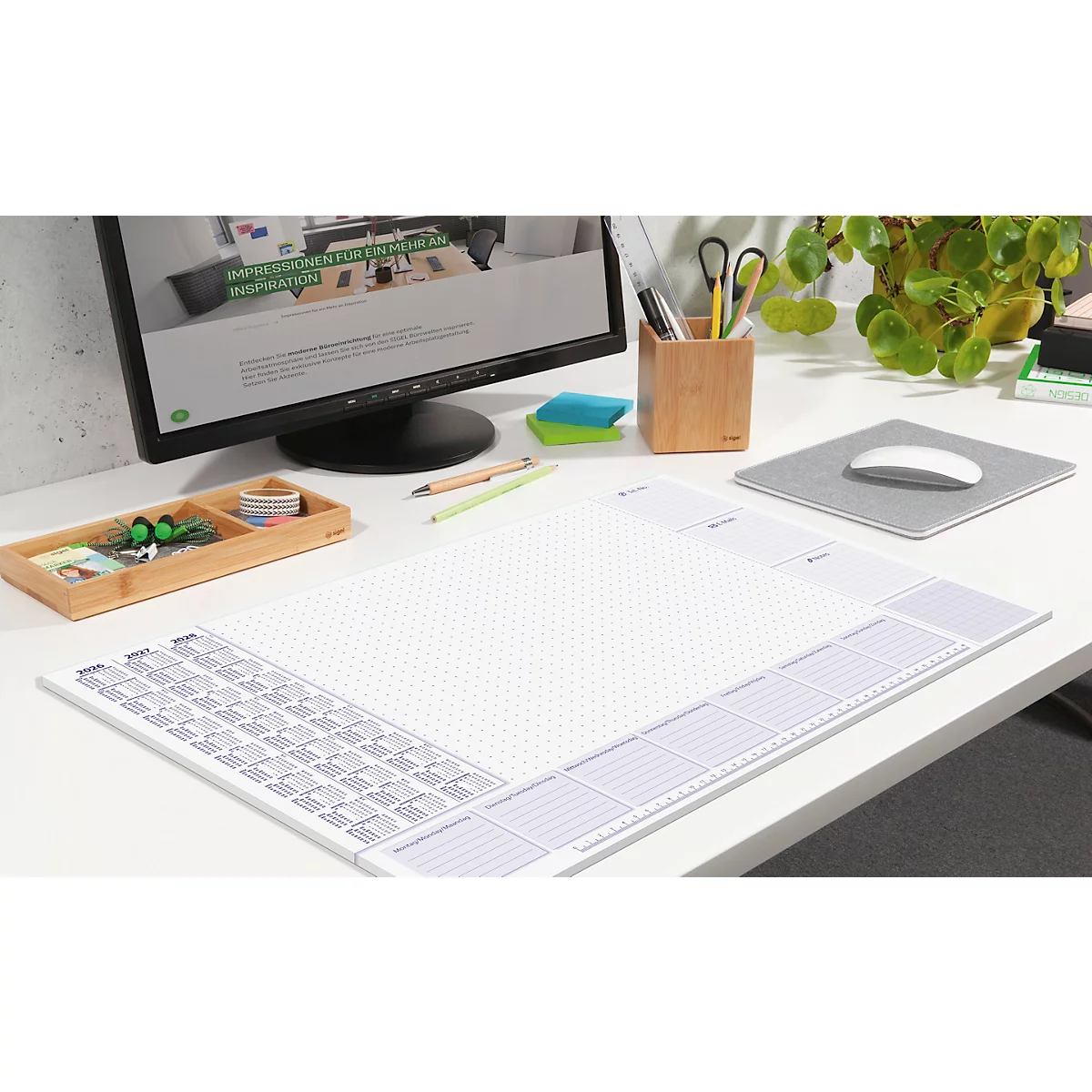 Schreibtisch mit Bürobedarf: Monitor, Schreibtischunterlage, Maus, Stiftehalter und Pflanzen.