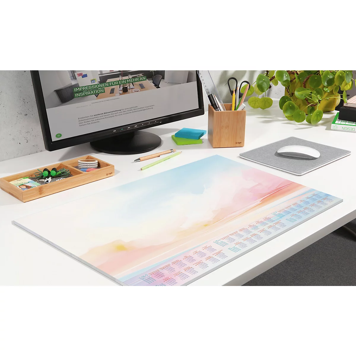 Schreibtisch mit bunten Unterlage, Tastatur-Design. Auf dem Tisch: Monitor, Stifte, Mauspad, Pflanzen. Helle, freundliche Atmosphäre.