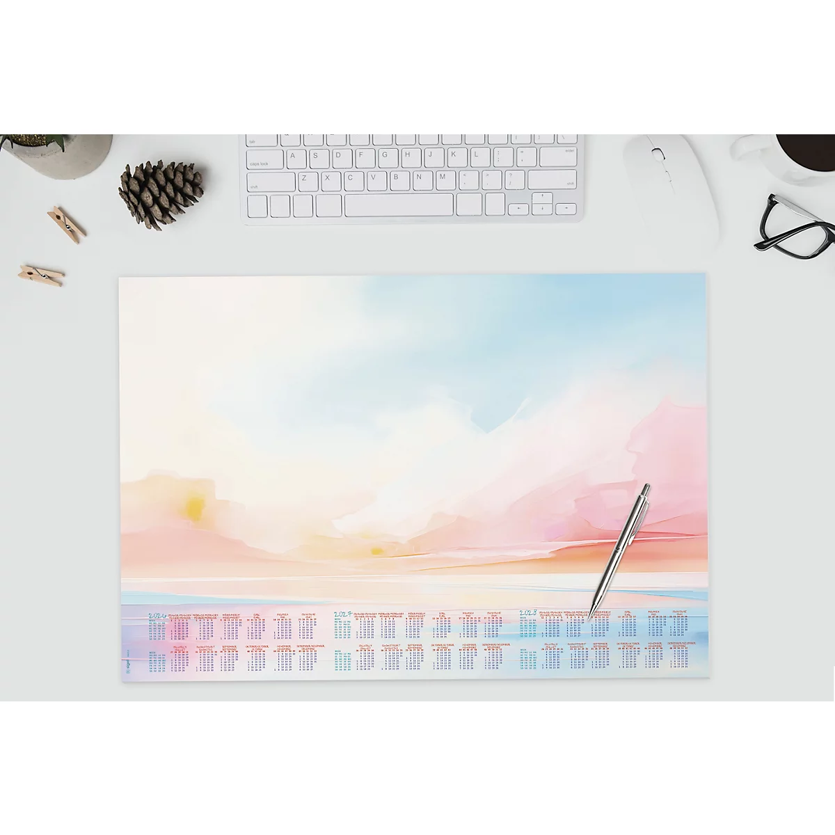 Schreibtischunterlage mit Aquarell-Himmelmotiv und Kalender. Silberner Stift liegt auf der Unterlage, neben einer Tastatur und einer Brille.