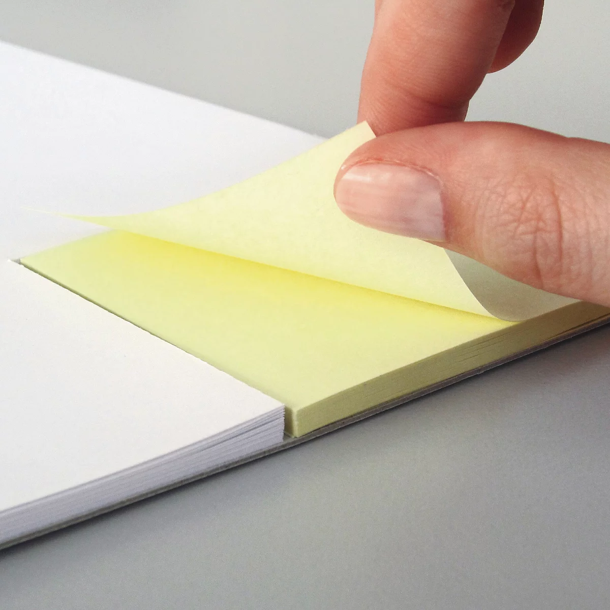 Eine Hand hebt ein gelbes Haftnotiz vom Block ab. Daneben liegt ein weisser Papierblock.