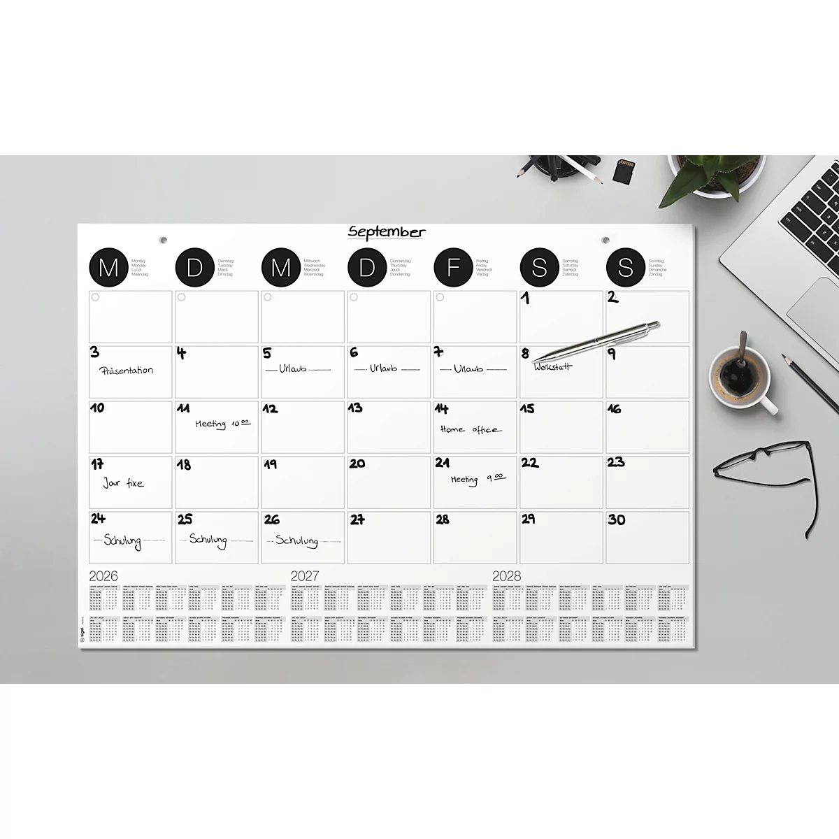Ein weisser Wandkalender für September, mit Terminen notiert. Daneben liegen eine Brille, ein Stift, eine Kaffeetasse und ein Laptop.