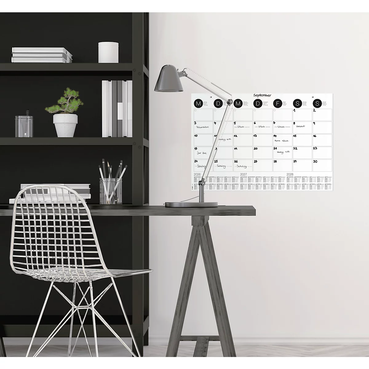Ein Schreibtisch mit Wandkalender, Schreibtischlampe und Stuhl. Auf dem Kalender sind die Wochentage von September 2019 zu sehen.