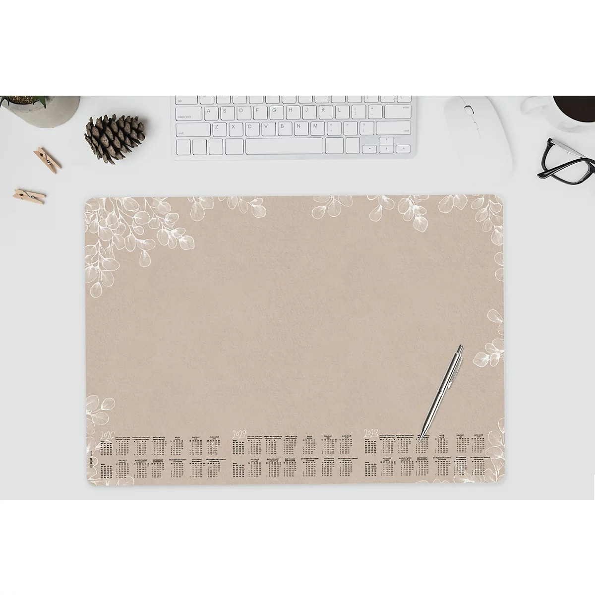 Schreibtischunterlage in Beige mit floralen Elementen und Jahreskalender. Eine silberne Kuli liegt auf der Unterlage.