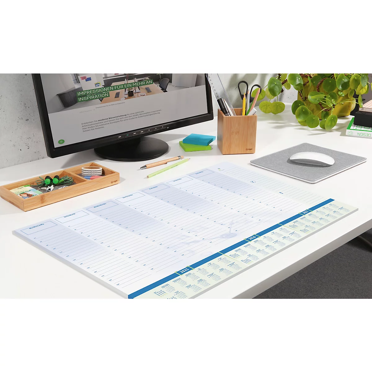 Ein Schreibtisch mit Wochenplaner, Computer und Büroausstattung. Der Planer ist im Fokus.