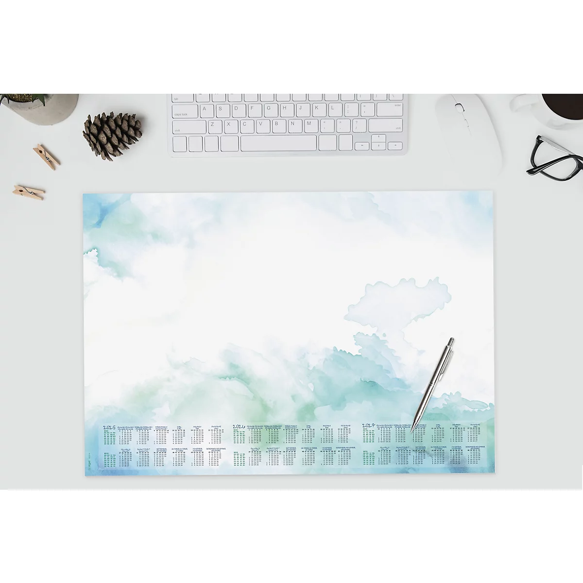 Schreibtischunterlage mit blau-grünen Aquarellflecken, darunter Jahreskalender. Stift liegt bereit.
