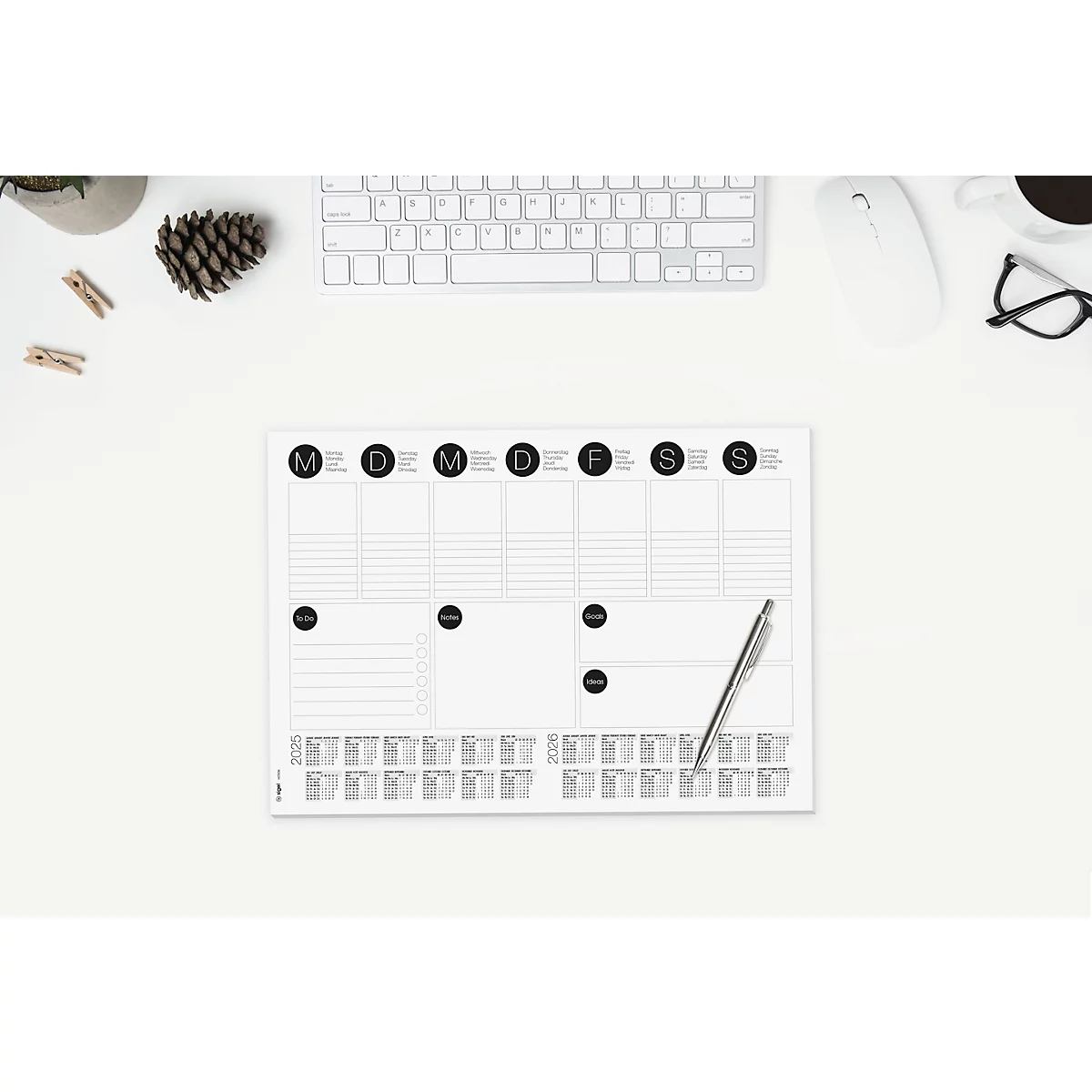 Draufsicht auf einen Schreibtisch. Ein Wochenplaner mit Stift, Tastatur, Maus, Brille, Kaffeetasse und Dekoartikel.