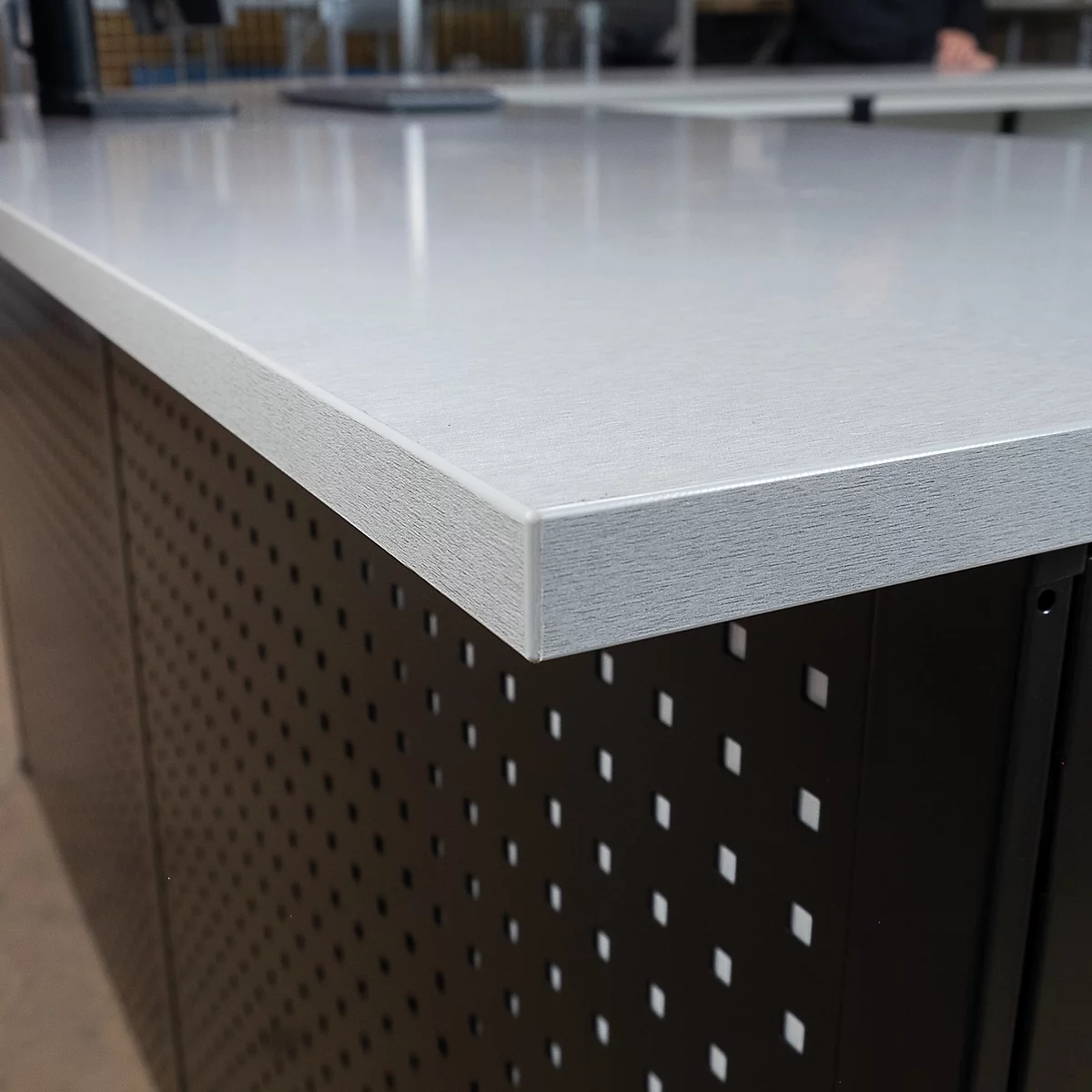 Gros plan d'un plateau de table avec une surface texturée. La table a un plateau gris et une base noire perforée.