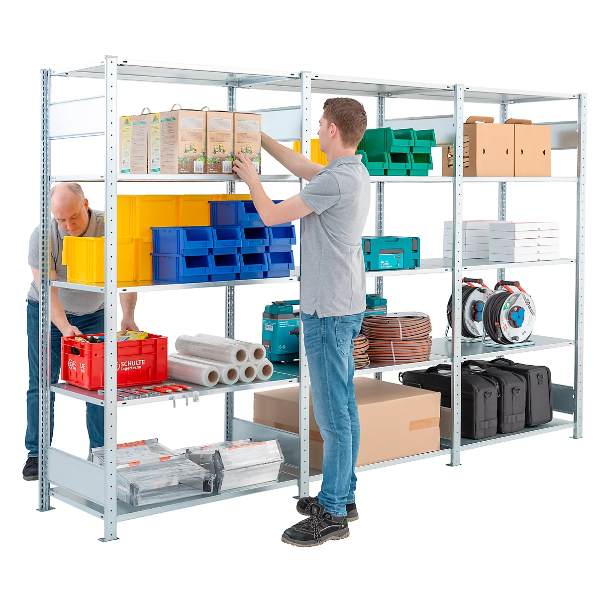 Deux hommes entreposent des marchandises dans une étagère métallique. Les étagères sont remplies de caisses, d'outils, de boîtes et de conteneurs.