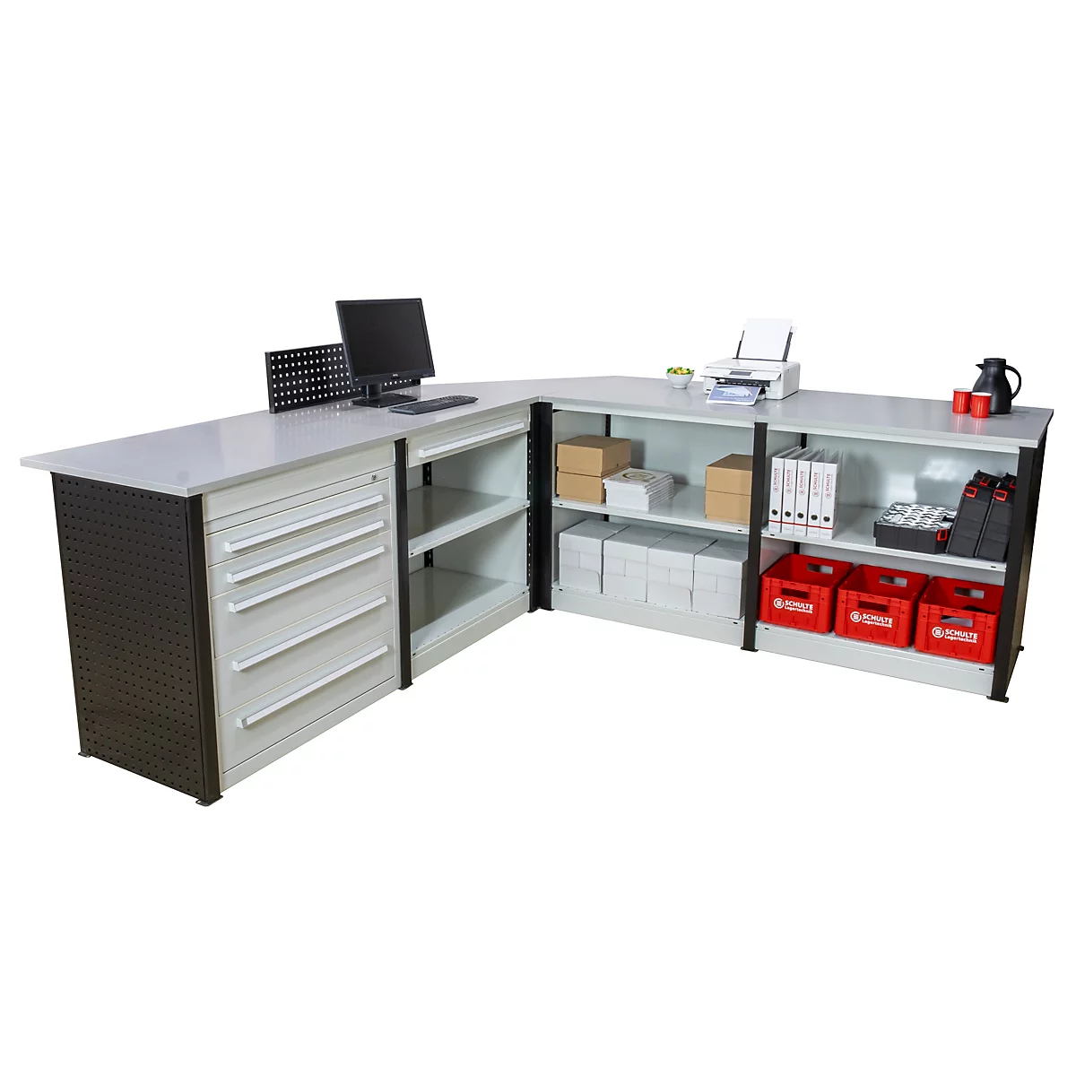 Een grote, witte L-vormige bureautafel. Op de tafel staan een computer, printer, ordners, dozen en kratten.