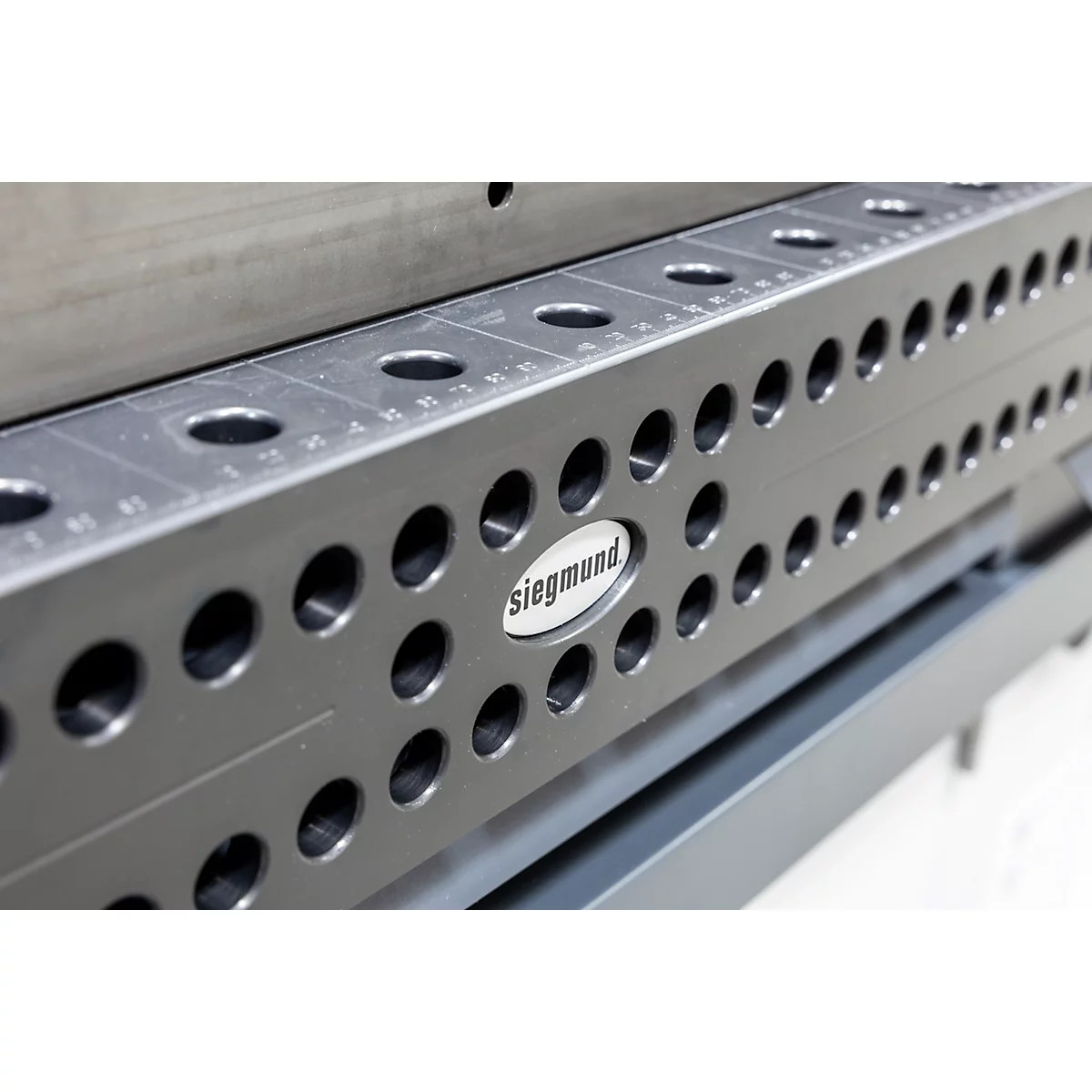 Detailaufnahme einer schwarzen Siegmund-Schweißtischkomponente mit kreisförmigen Löchern und Skalen. Das Logo 'Siegmund' ist prominent.