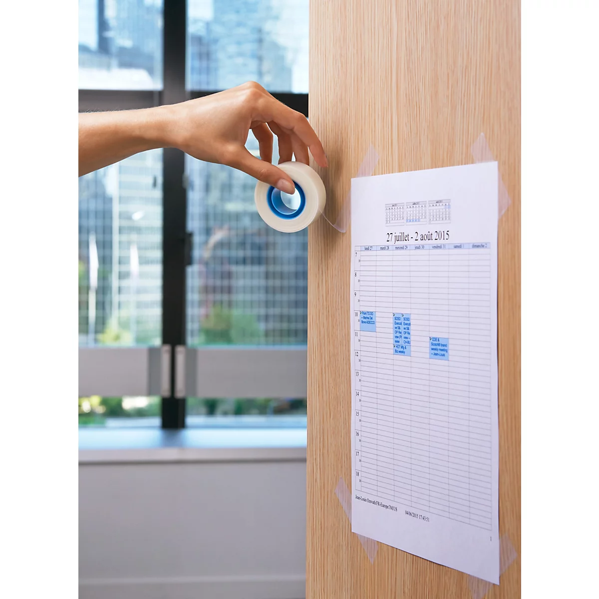 Hand klebt Notiz an Holzwand mit Klebeband. Fenster im Hintergrund.