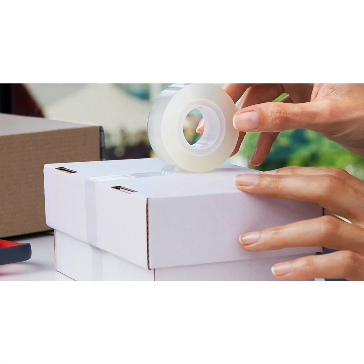 Handen plakken een wit pakket dicht met een rol transparante Scotch-tape.
