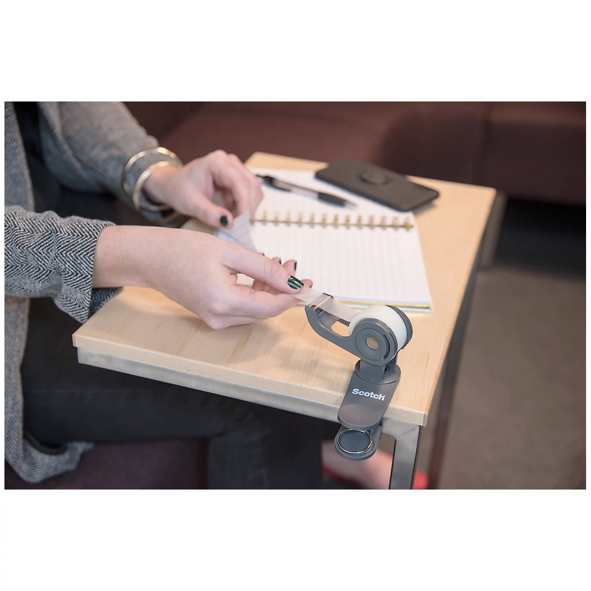 Person cutting tape with a tape dispenser on a table. Beside it notebook, pen and mobile phone.