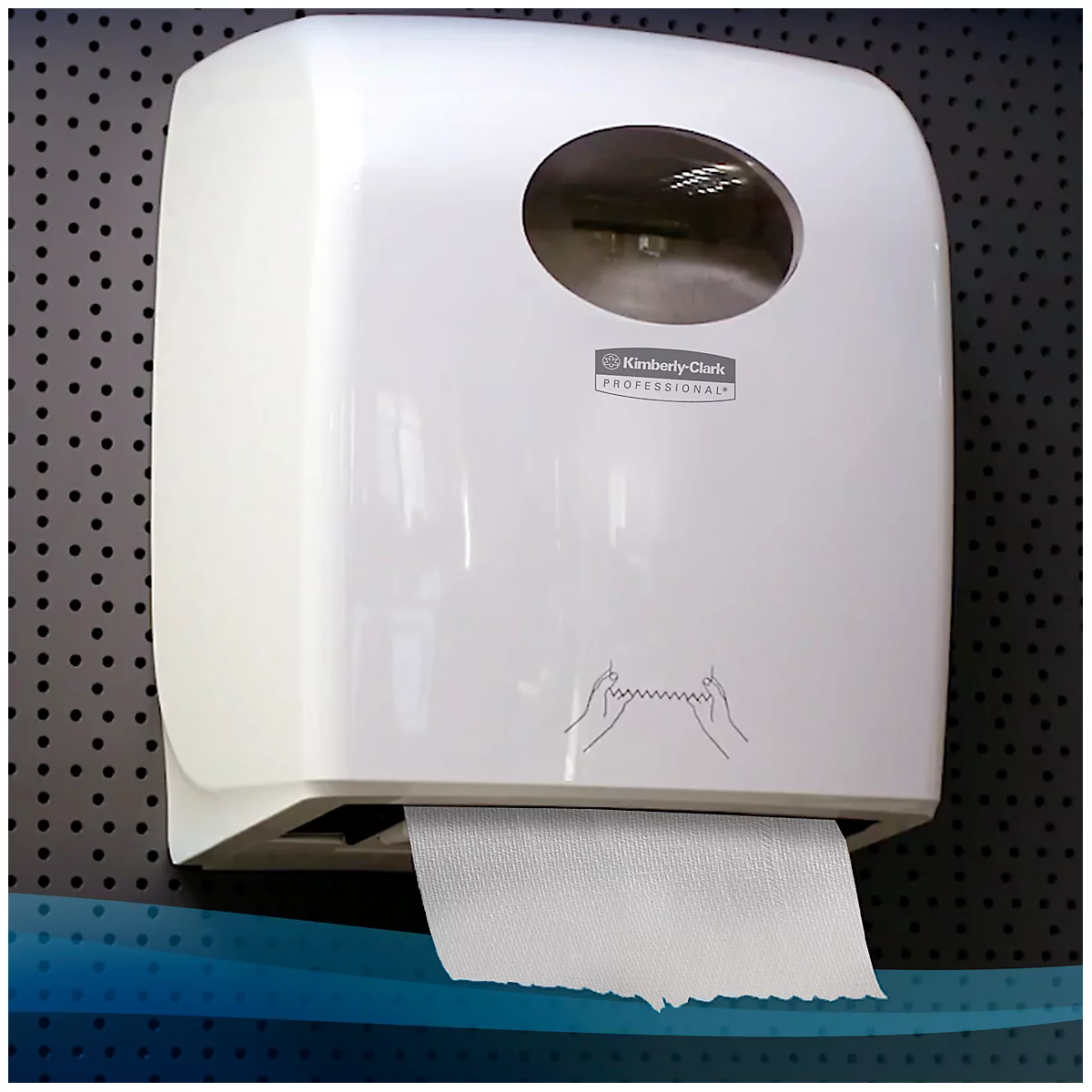 Weisser Papierhandtuchspender an einer Wand. Ein Papierhandtuch hängt heraus. Auf dem Spender steht "Kimberly-Clark Professional".