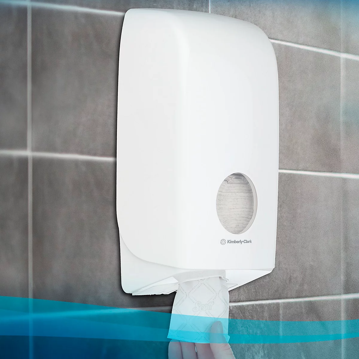 Witte papieren handdoekdispenser aan een grijze muur. Er wordt een vel papier gepakt. De tekst "Kimberly Clark" is zichtbaar.