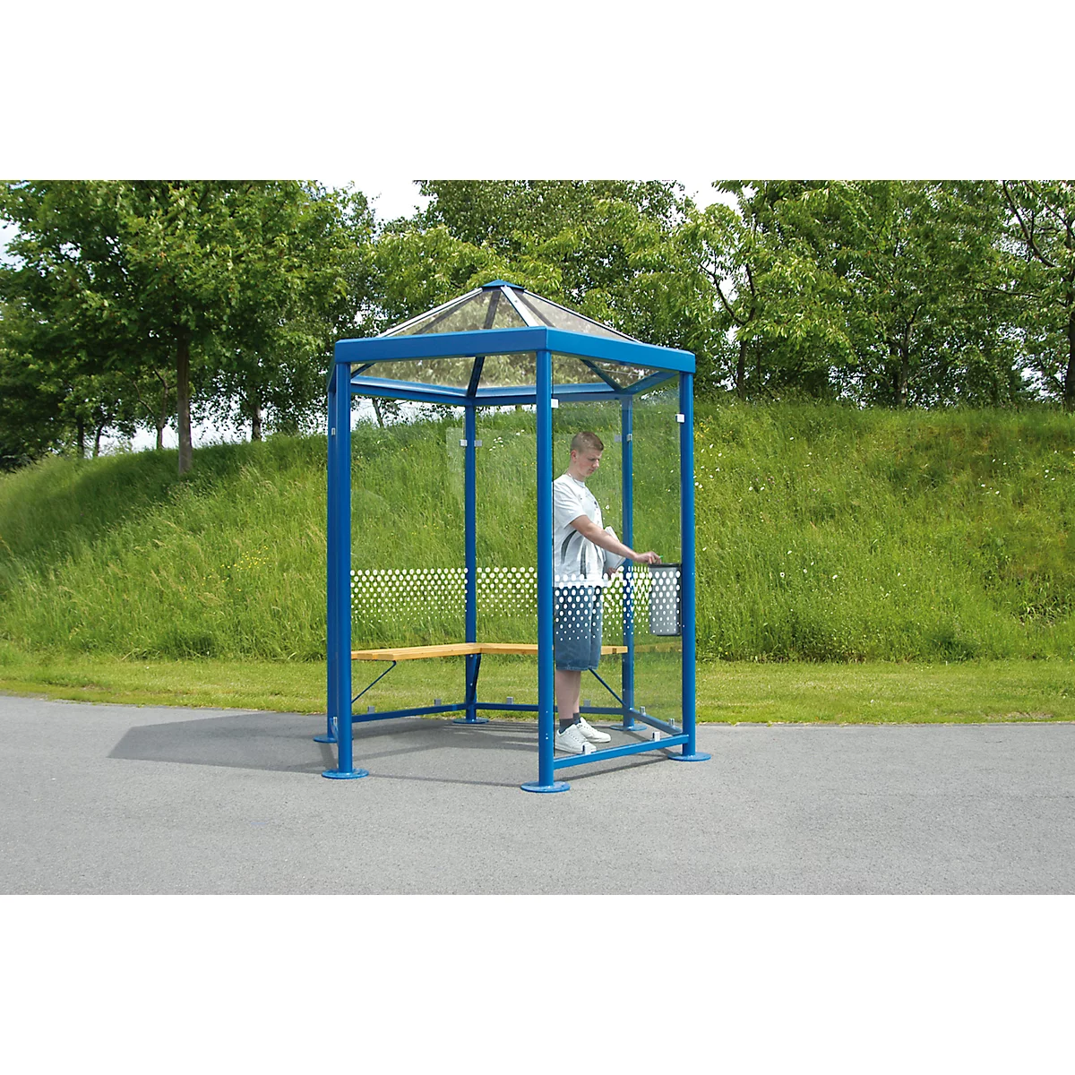 Blau-transparenter Wartehäuschen mit Mann, Wald im Hintergrund.