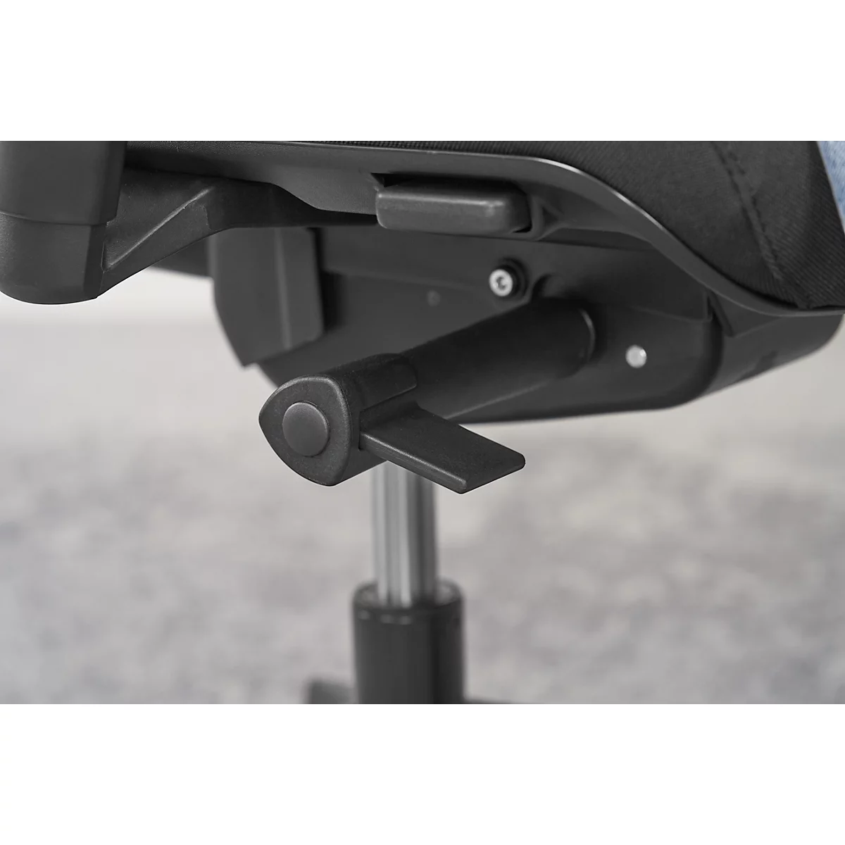 Close-up of a black chair mechanism with lever, dial and metal bar, against a gray background.