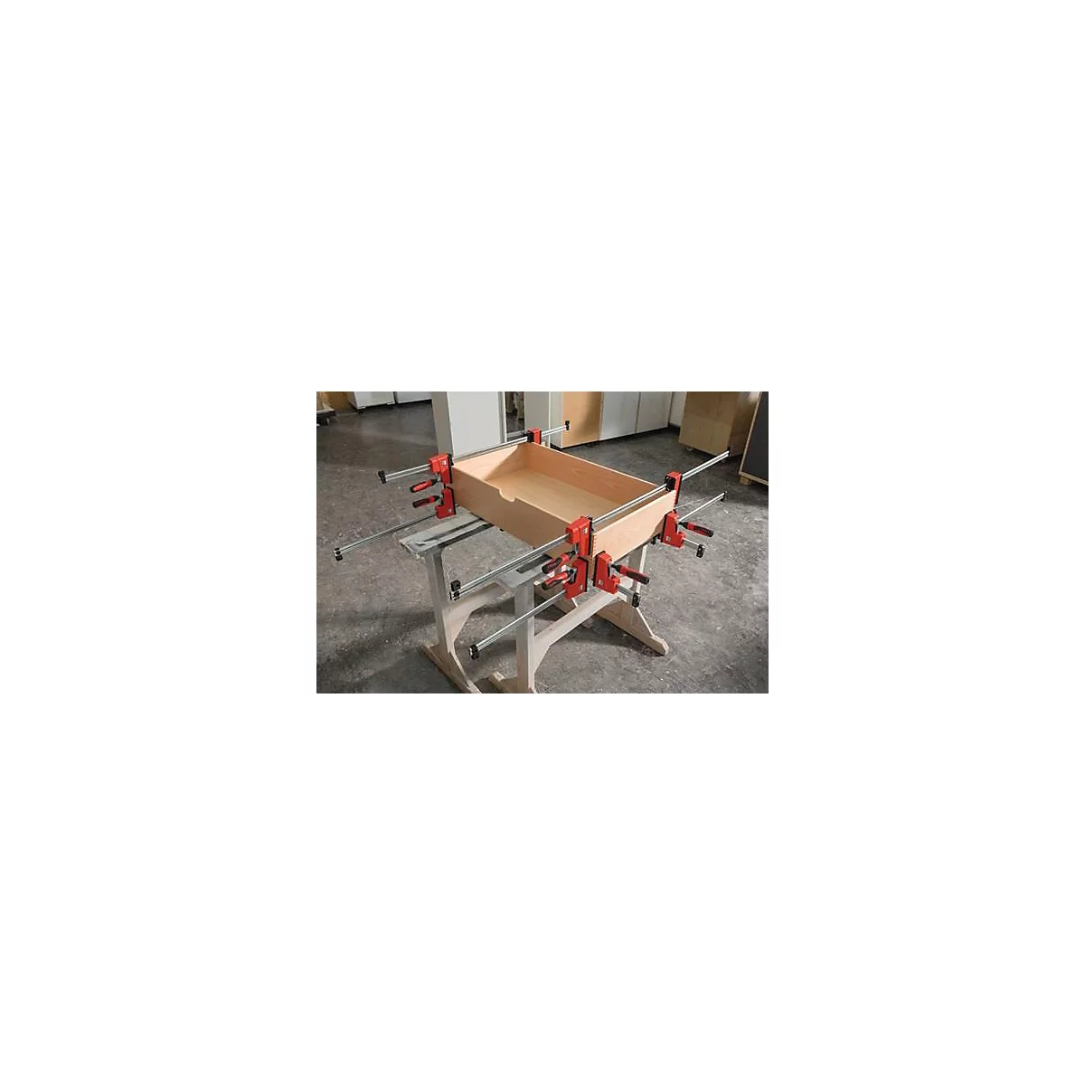 Caisse en bois fixée avec des serre-joints sur un établi. Boîte en bois, serre-joints rouge-noir, tiges métalliques, surface en bois clair.