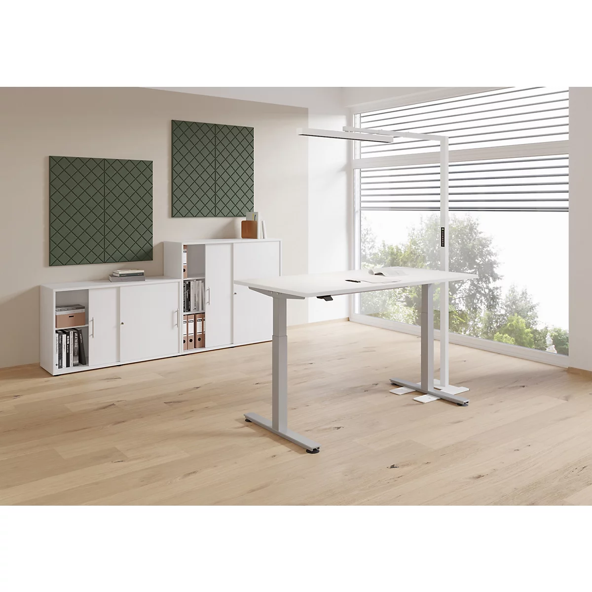 Un bureau réglable en hauteur se trouve dans un bureau avec une grande fenêtre. Un lampadaire à droite. Des armoires en arrière-plan.