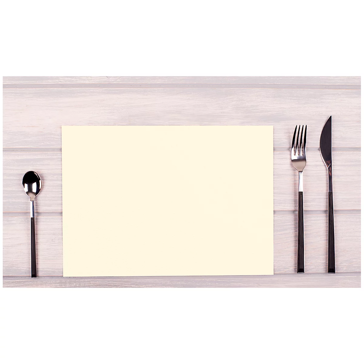 Couvert avec papier vierge, cuillère à gauche, couteau et fourchette à droite sur bois clair.