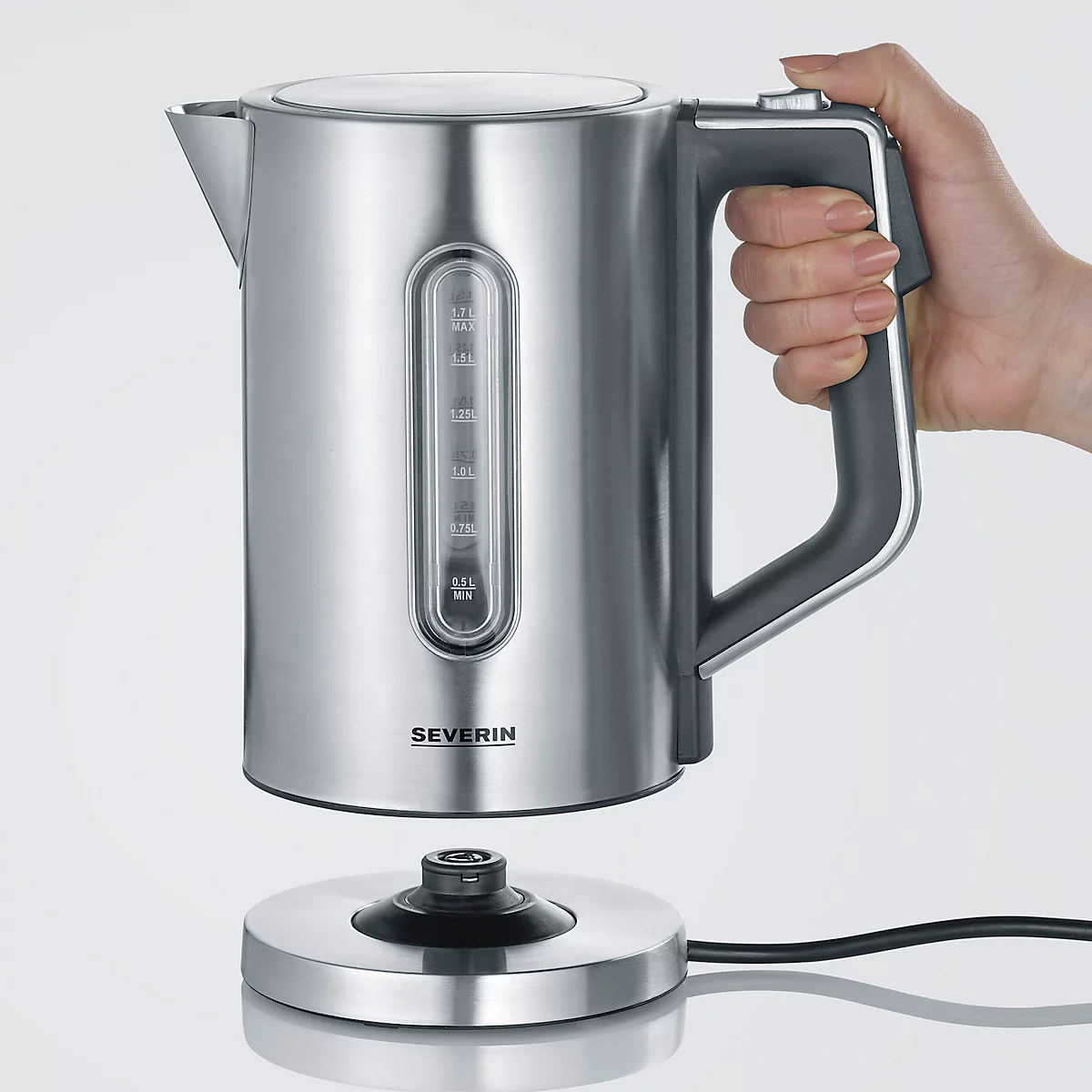 A silver kettle floats above its base, held by a hand. A black handle and a viewing window can be seen.