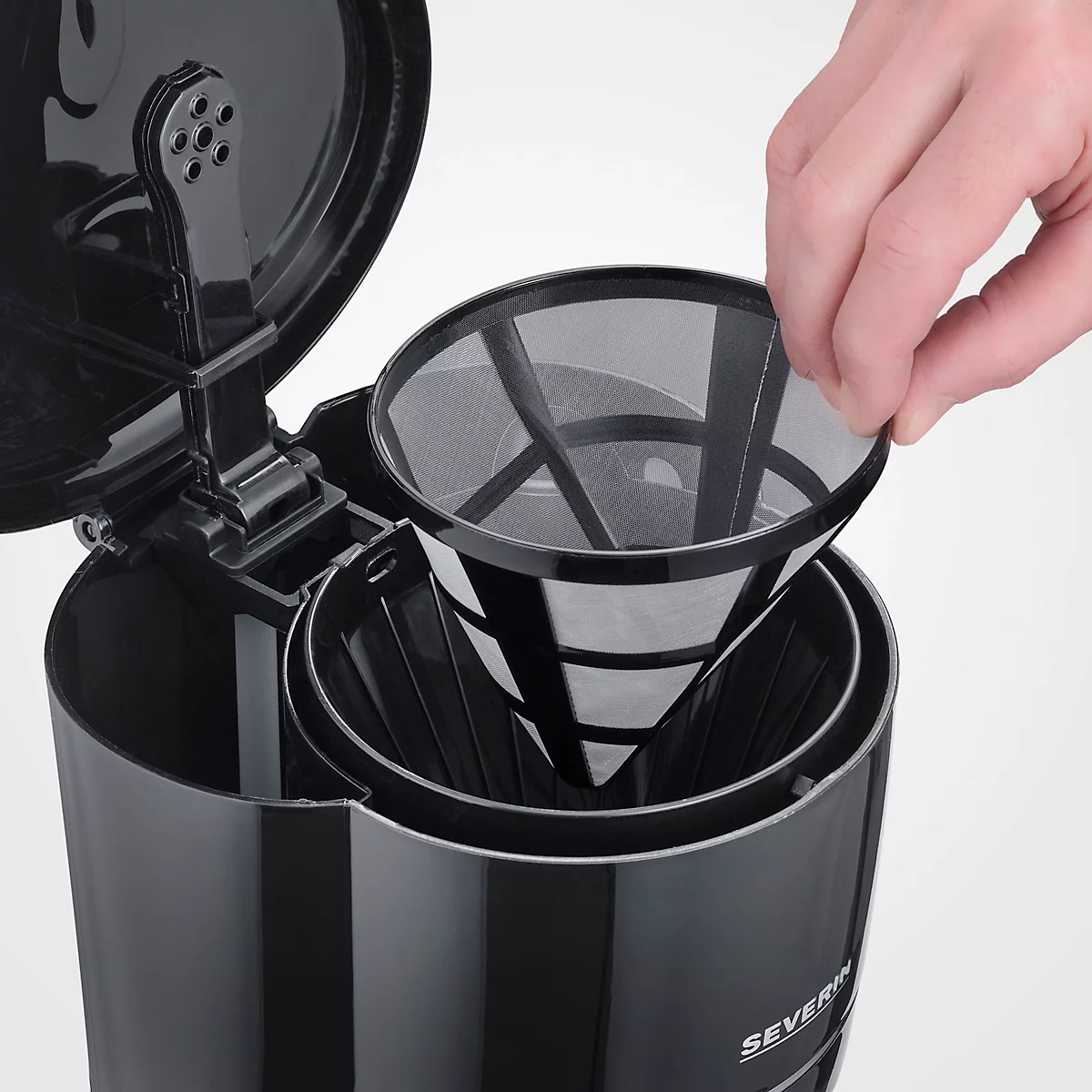Nahaufnahme einer schwarzen Kaffeemaschine mit eingesetztem Filter. Eine Hand hält den Filter.