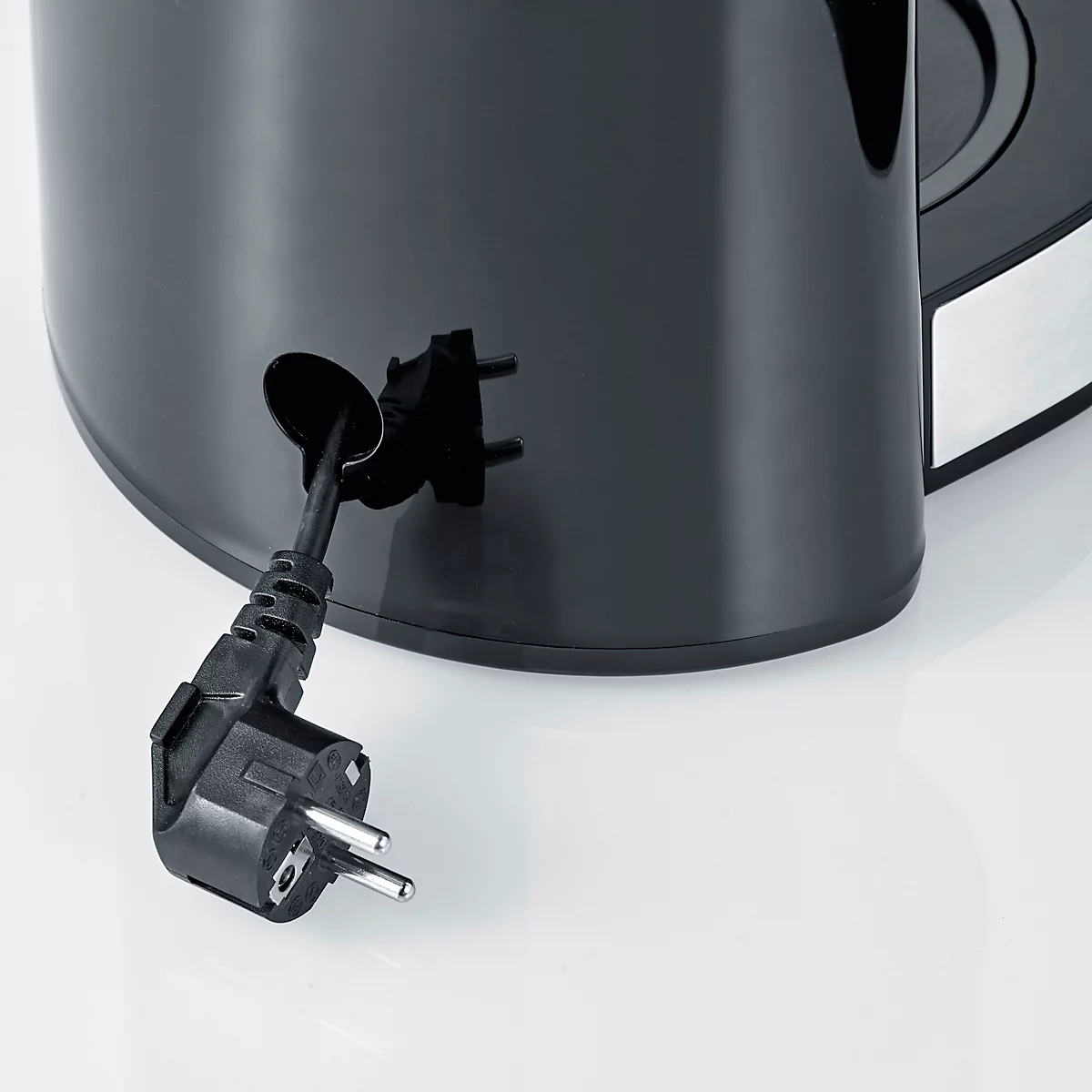 Detailaufnahme: Schwarzer Stecker ragt aus Kaffeemaschine. Der Stecker wird durch ein Loch geführt. Hintergrund ist hellgrau.