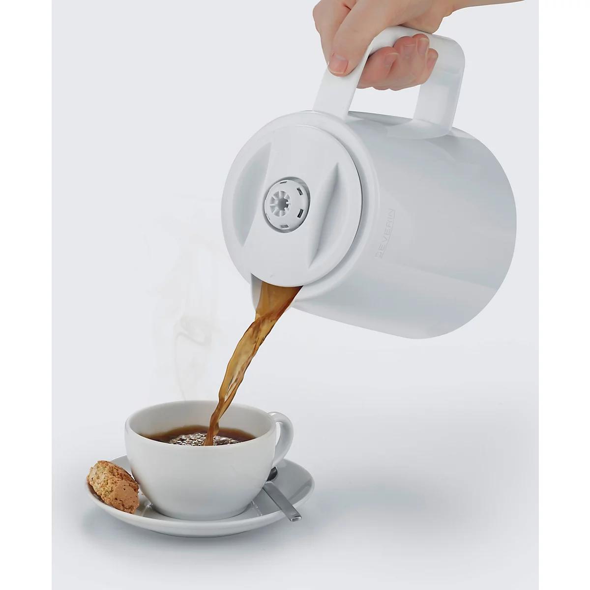 Eine weiße Kaffeekanne gießt Kaffee in eine Tasse. Auf dem Unterteller liegen Keks und Löffel.