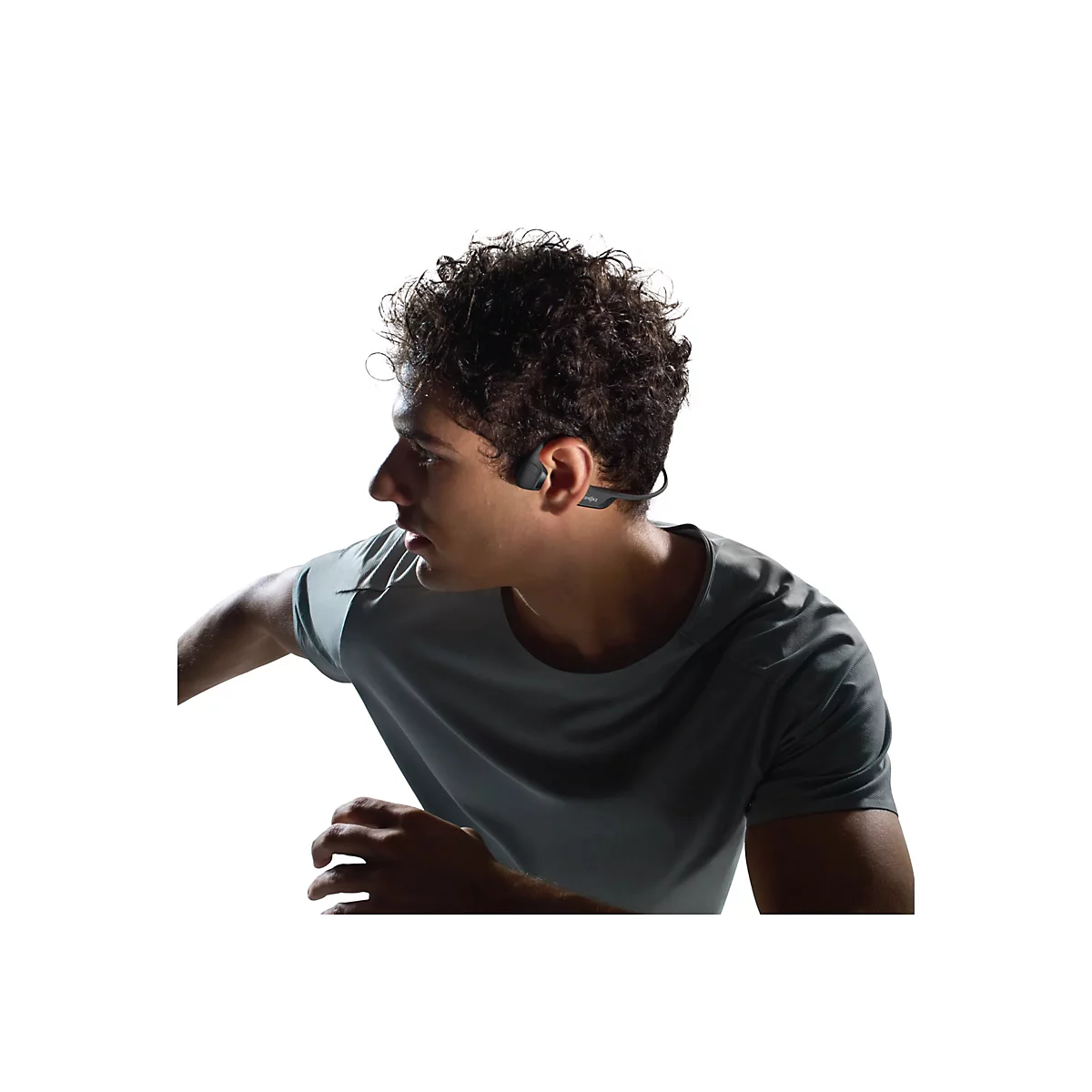 Mann mit lockigem Haar, trägt Sport-Kopfhörer. Er scheint gerade zu rennen, ein graues T-Shirt tragend, vor weissem Hintergrund.
