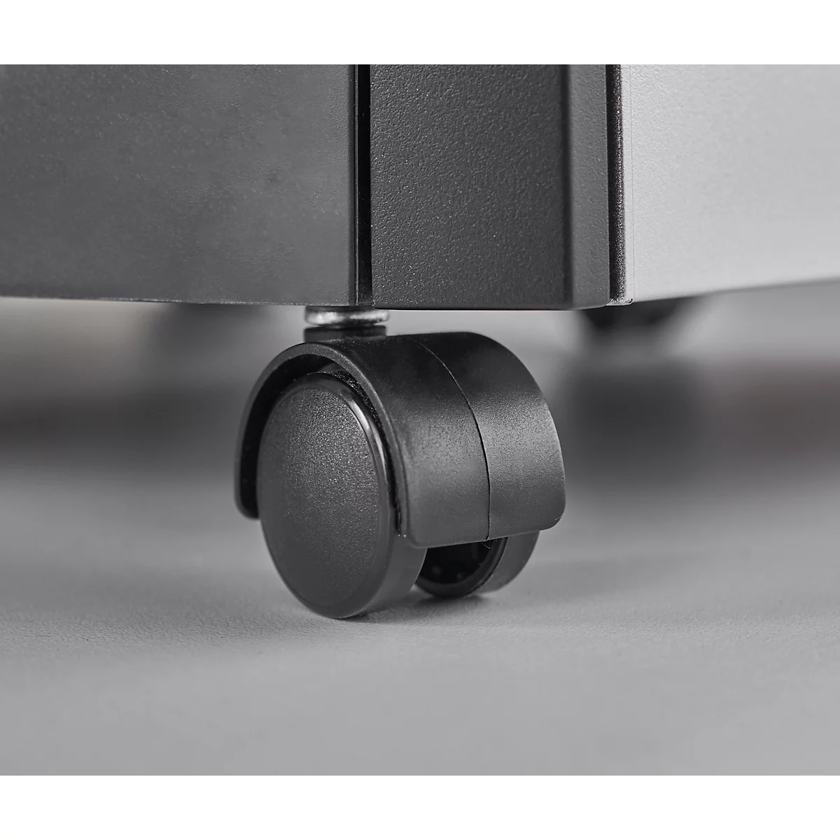 Close-up of a black caster wheel attached to a piece of furniture. The background is blurred and gray.