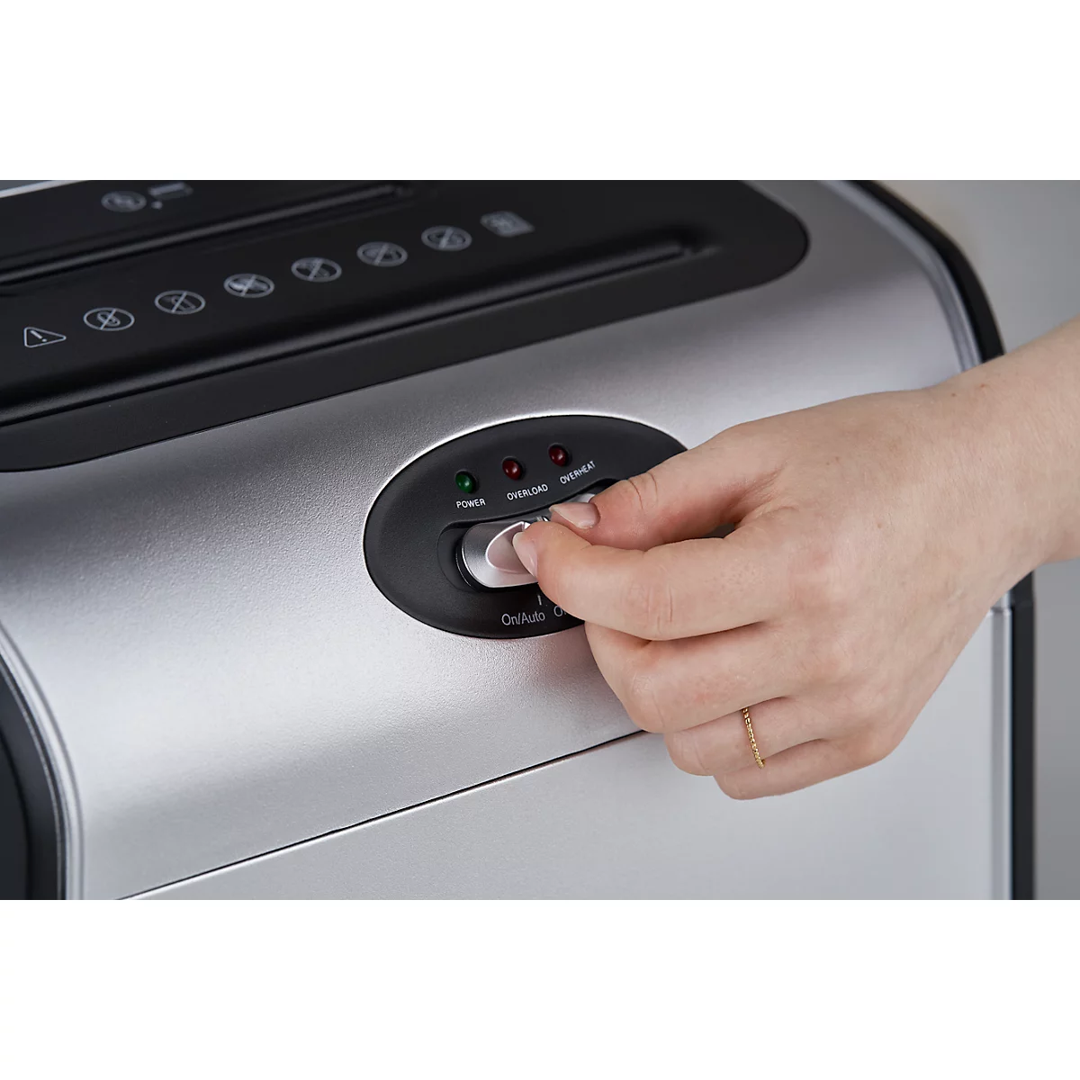 Hand turning a button on a shredder. Lights are illuminated on the control panel.