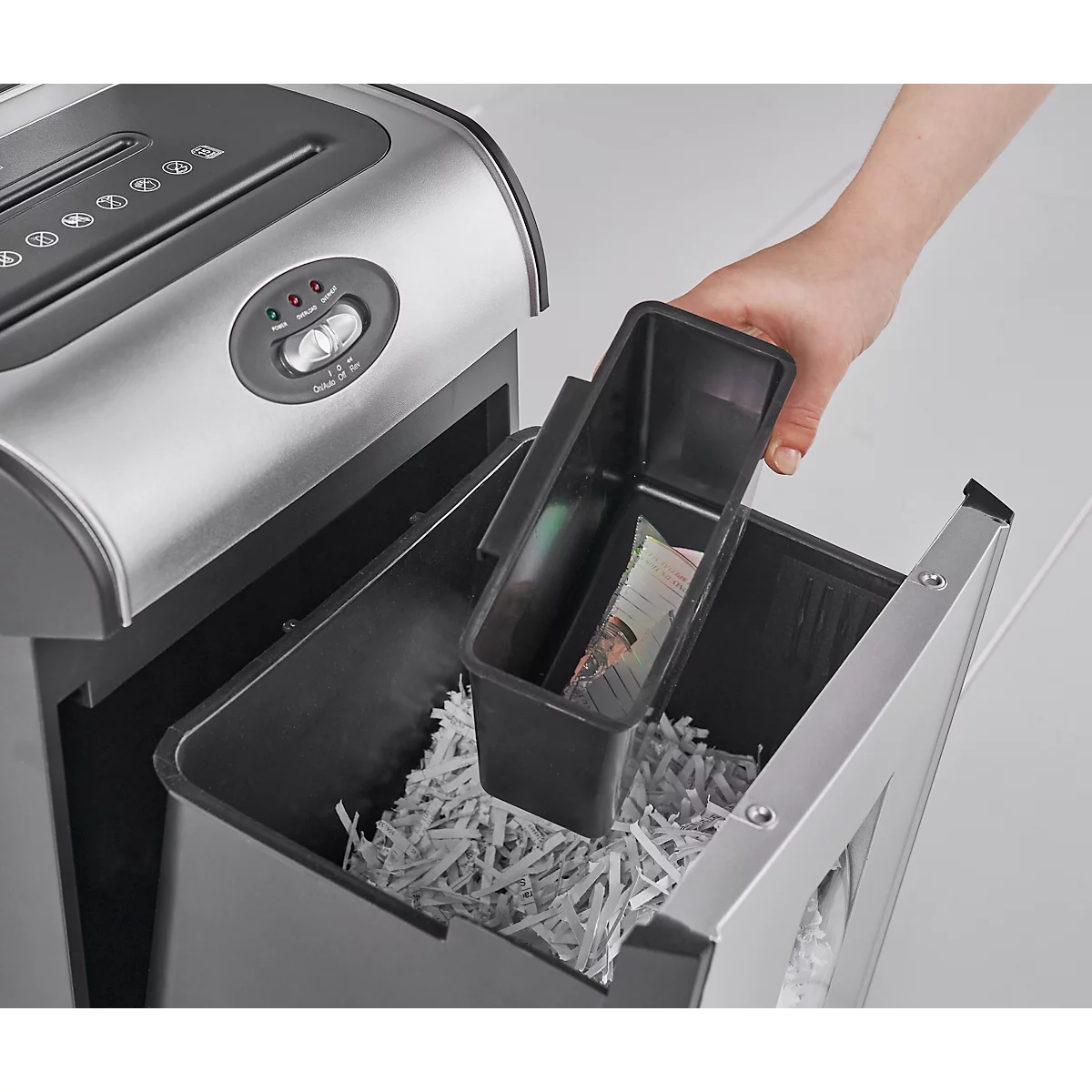 Close-up of a paper shredder. A hand lifts a black container filled with shredded paper out of a larger container.